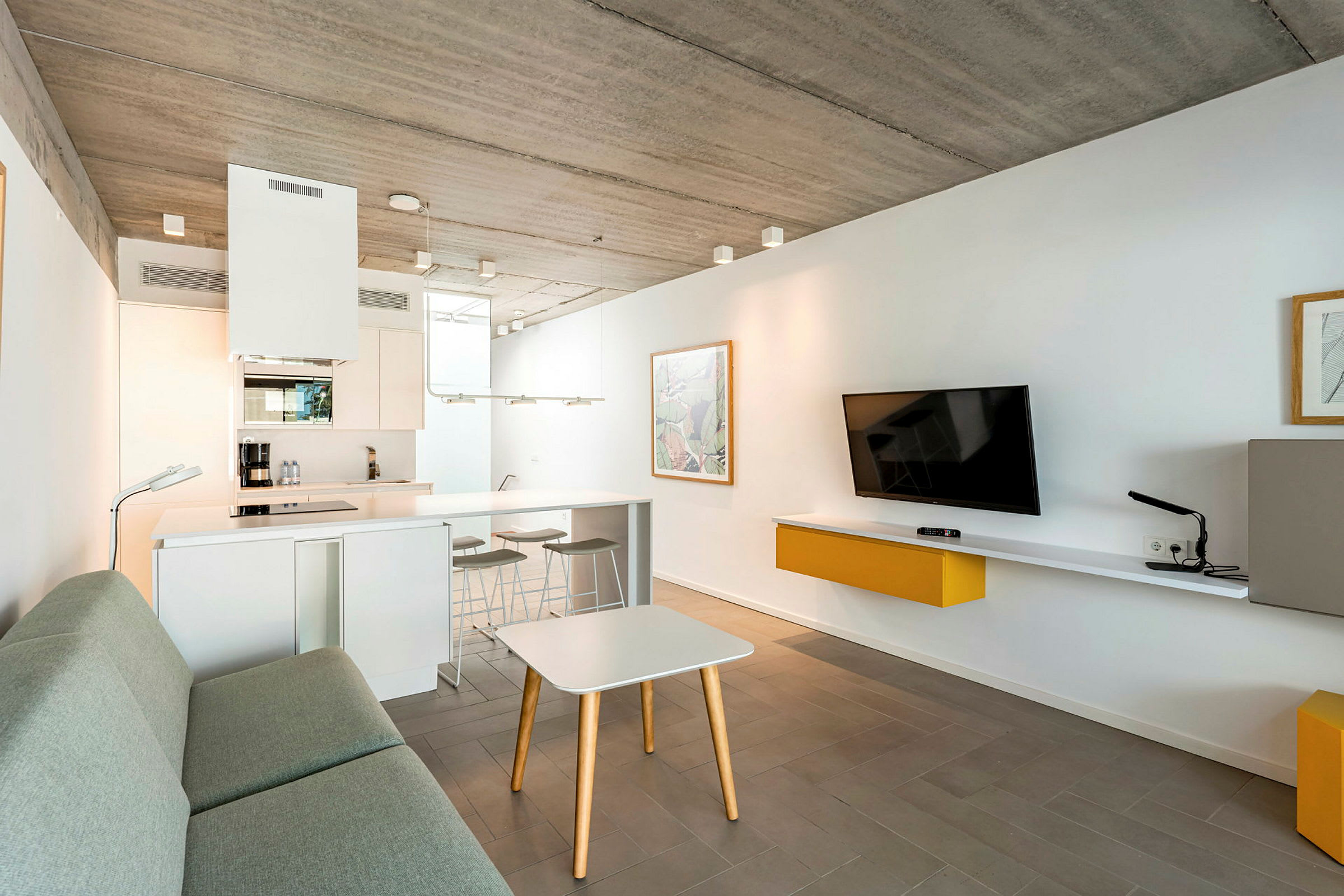 Ett modernt, minimalistiskt vardagsrum med köksdel och grå soffa. (AI-genererad text)