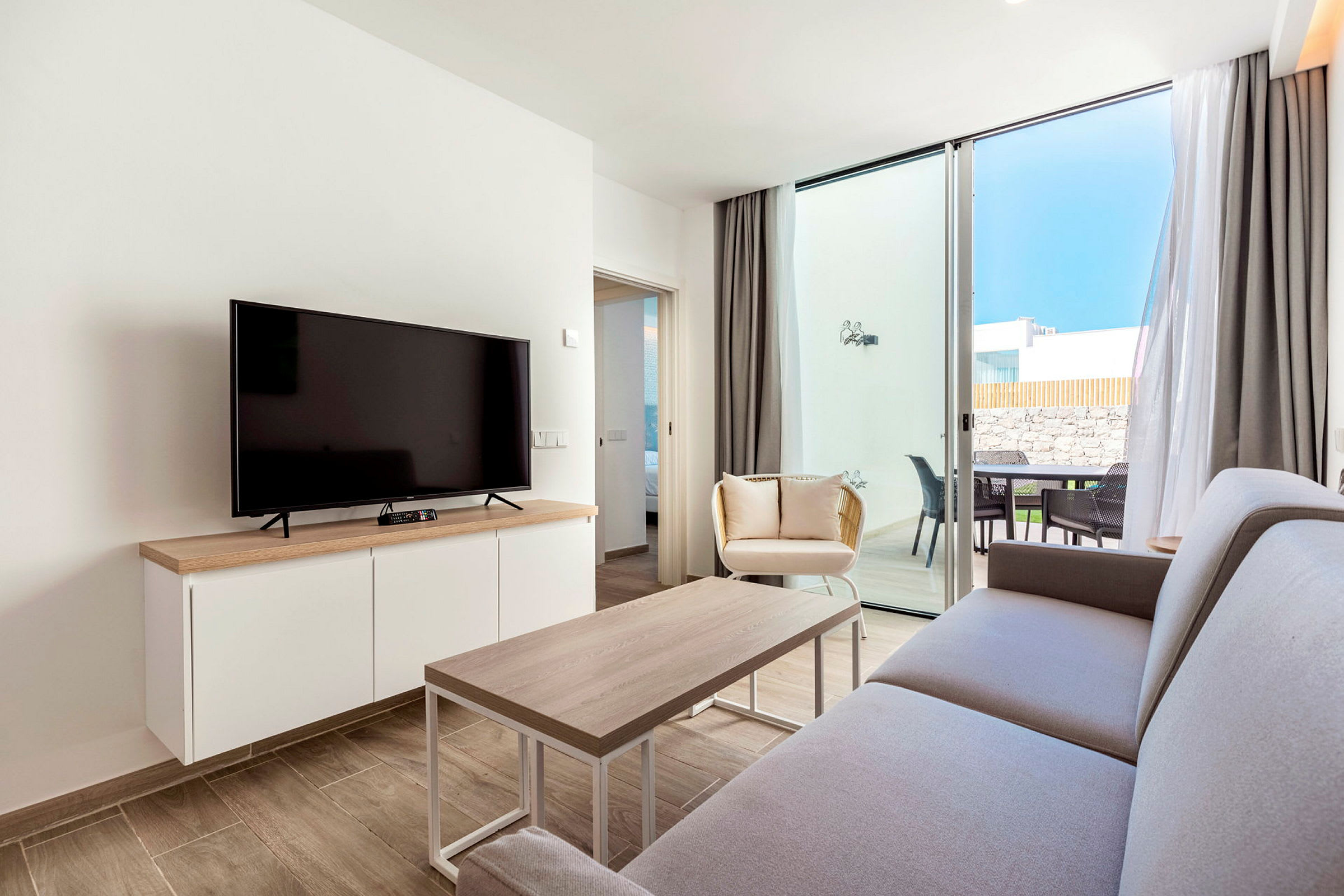 Ett modernt vardagsrum med en soffa, soffbord, TV och fönster som öppnar sig mot en terrass. (AI-genererad text)