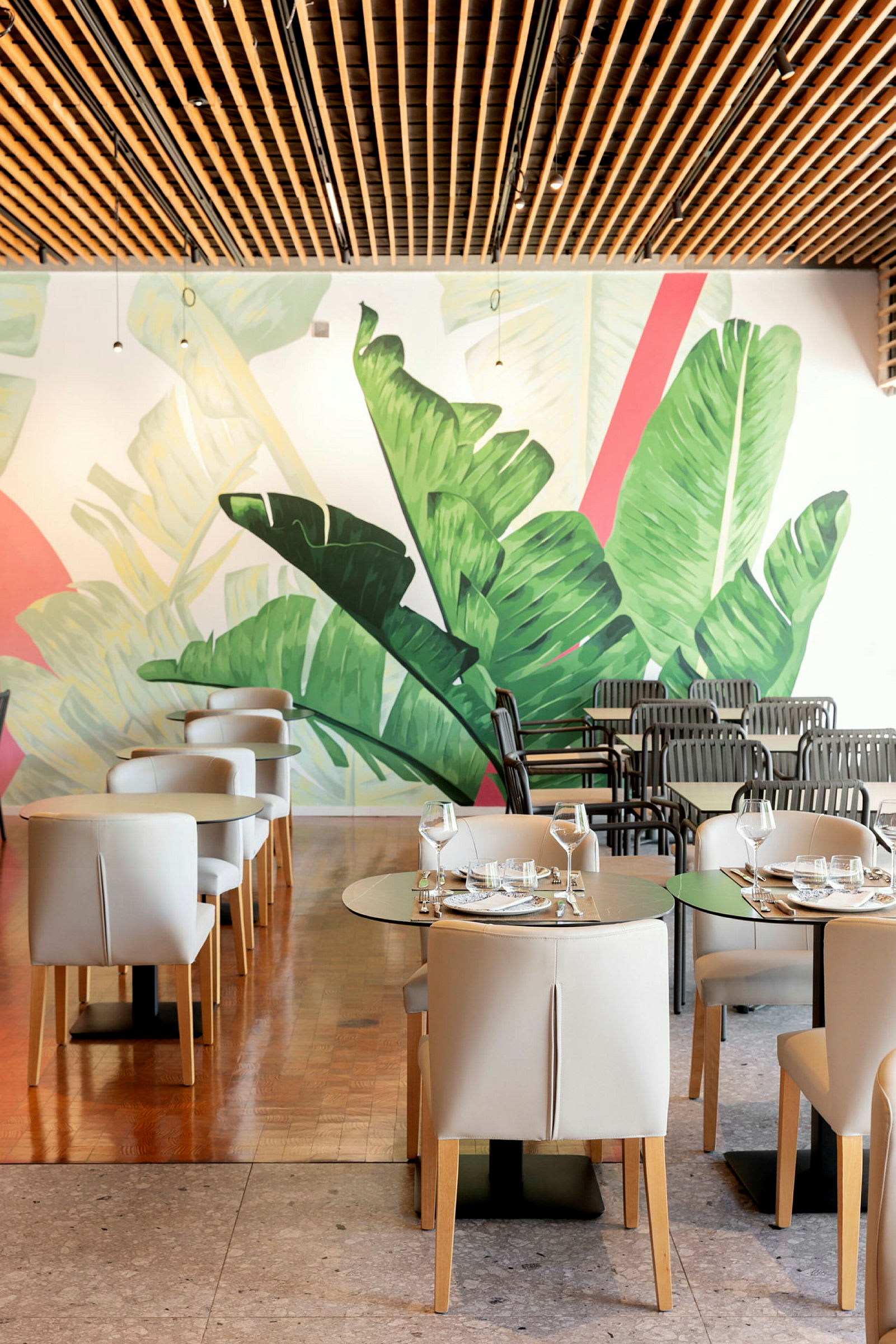 Restaurangmiljö med moderna möbler och en väggmålning av stora gröna löv. (AI-genererad text)