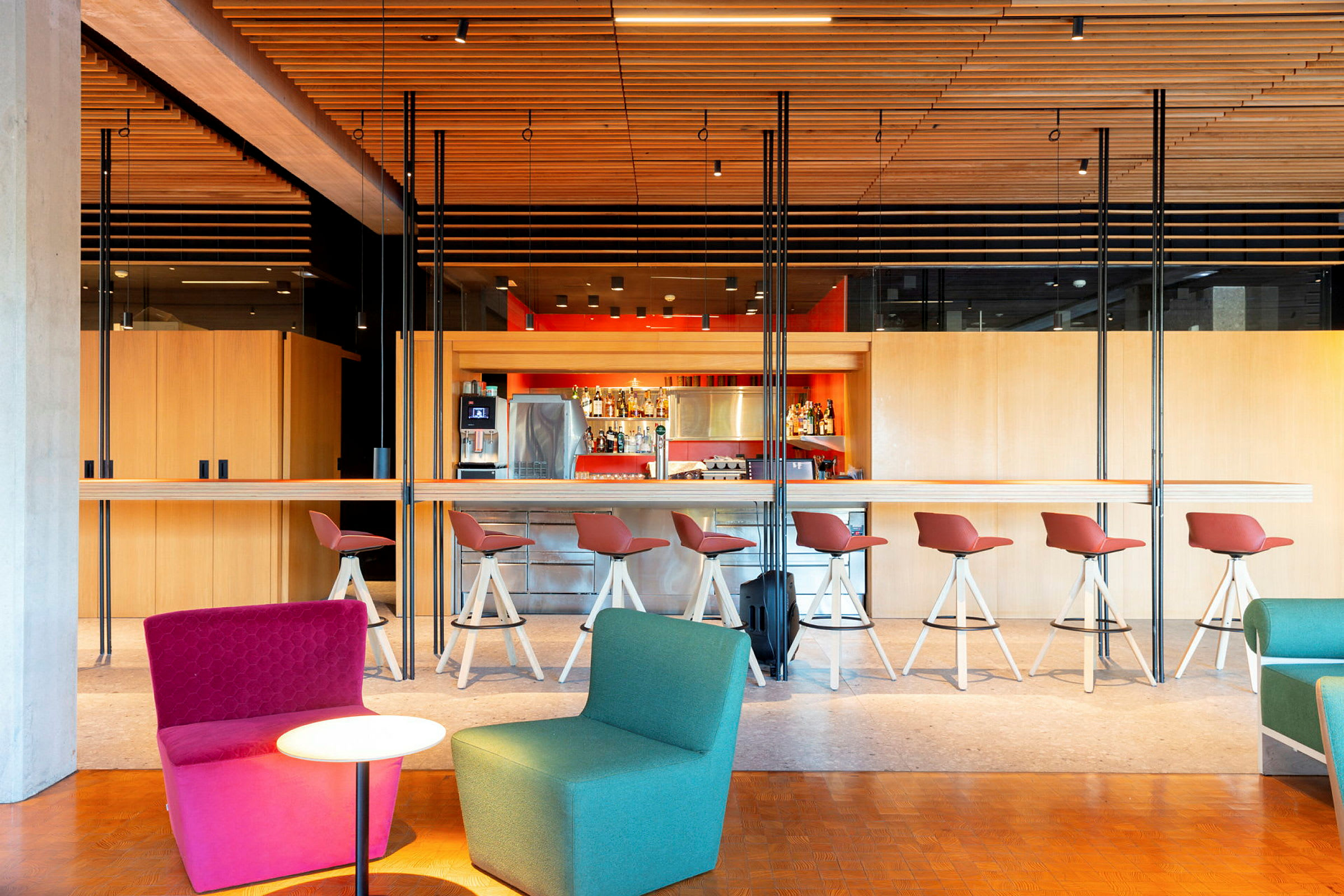 Modern bar med höga röda stolar och några bekväma fåtöljer i förgrunden. (AI-genererad text)