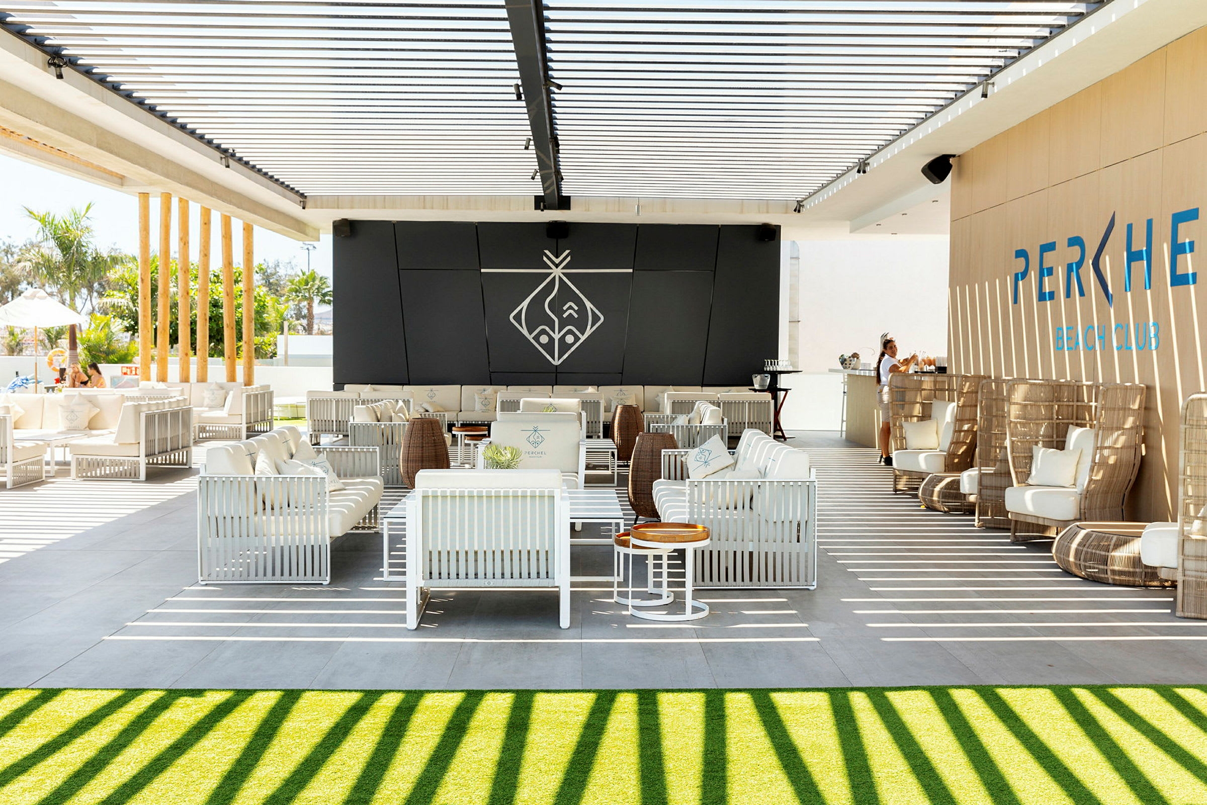En utomhuslounge med vita sittmöbler och en bar under en pergola med skuggning. (AI-genererad text)