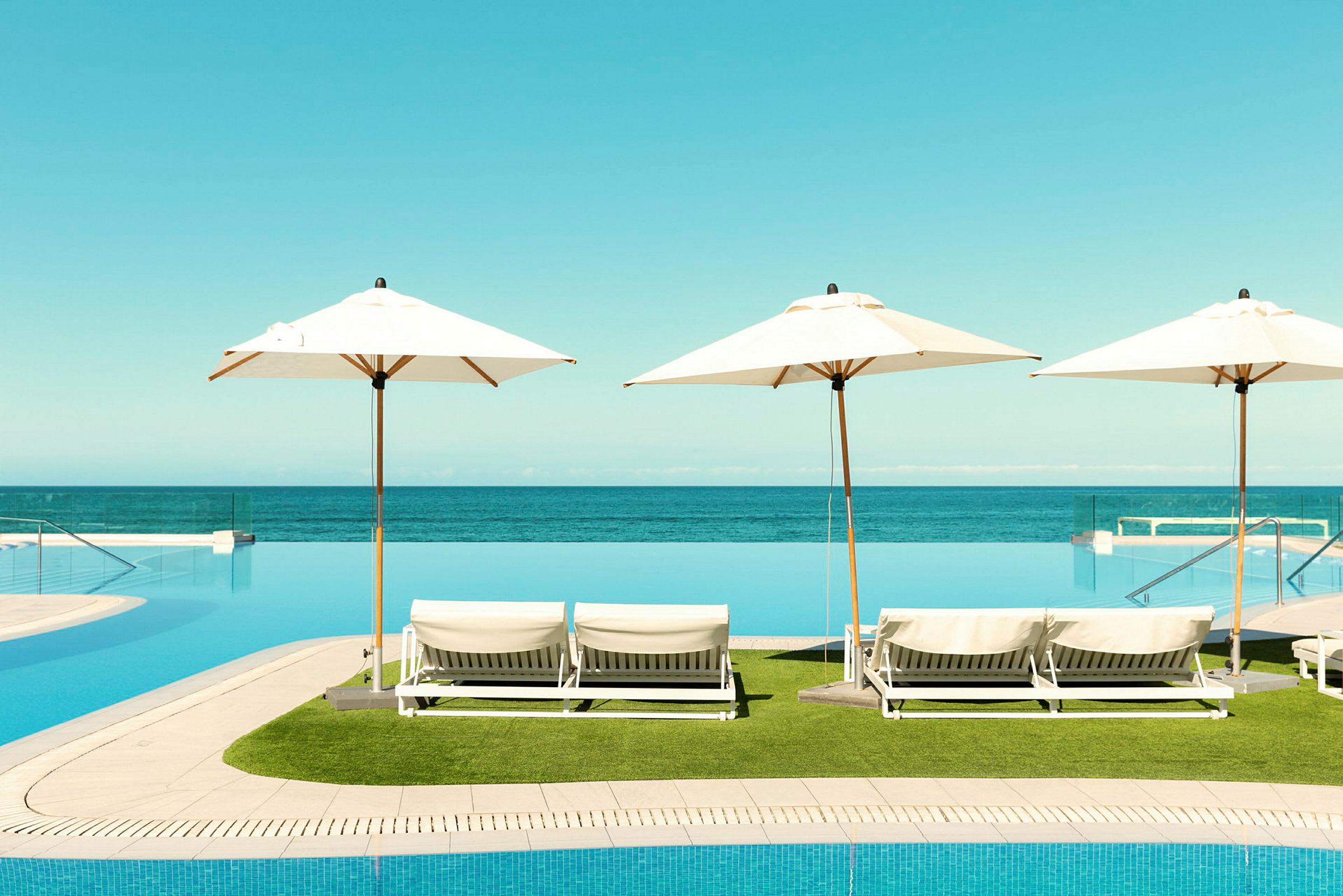 Vy av solstolar med parasoller vid en infinitypool, havet i bakgrunden. (AI-genererad text)