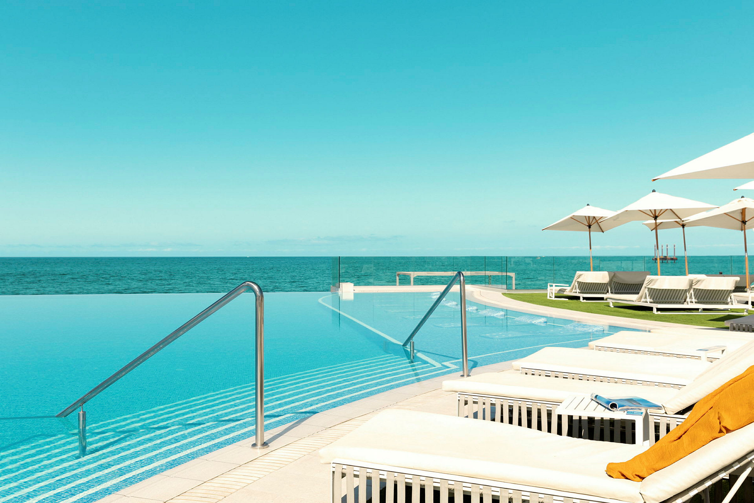 En infinitypool med utsikt över havet, omgiven av solstolar och parasoller. (AI-genererad text)