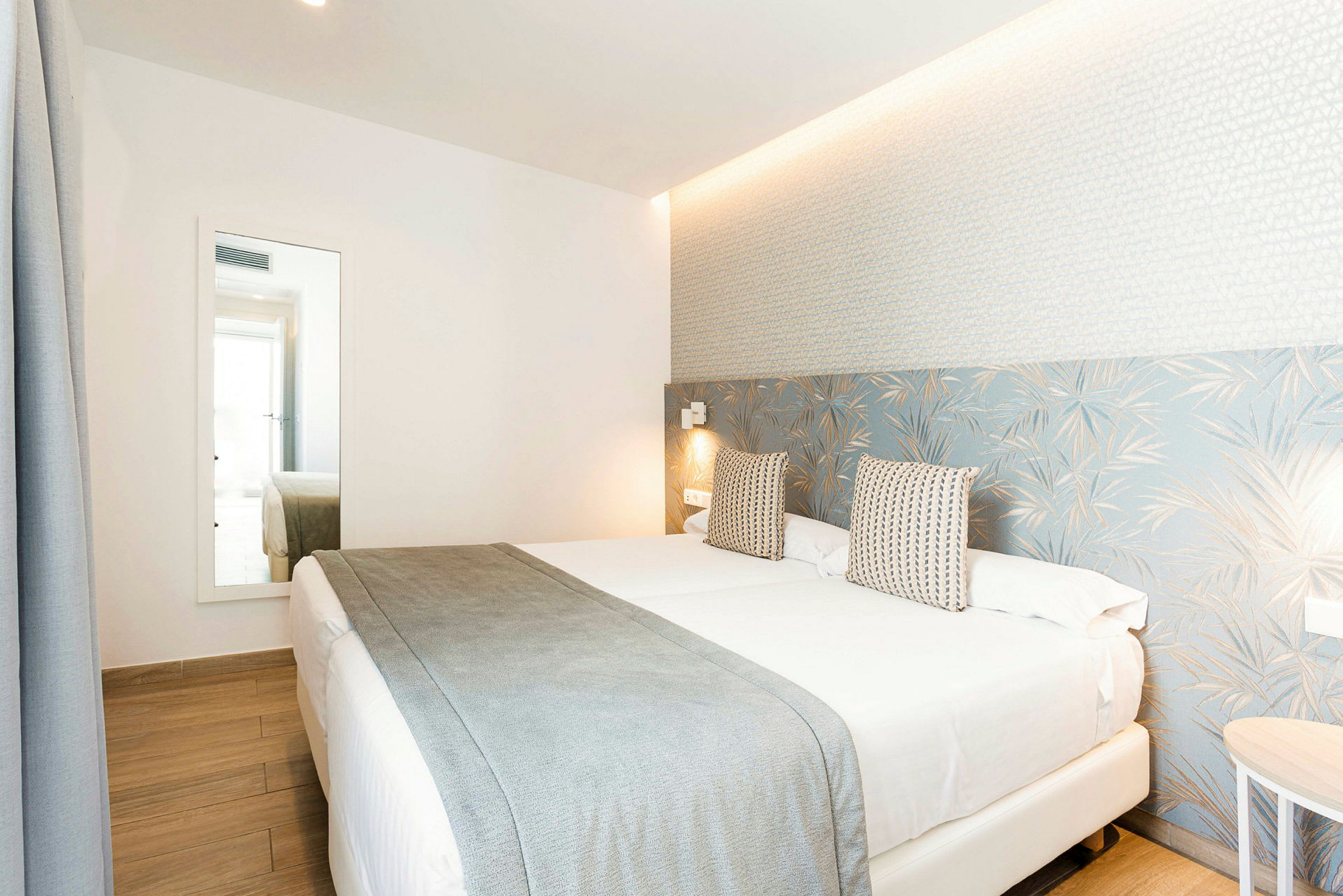 Hotellrum med en dubbelsäng, ljus inredning och ett stort spegel. (AI-genererad text)