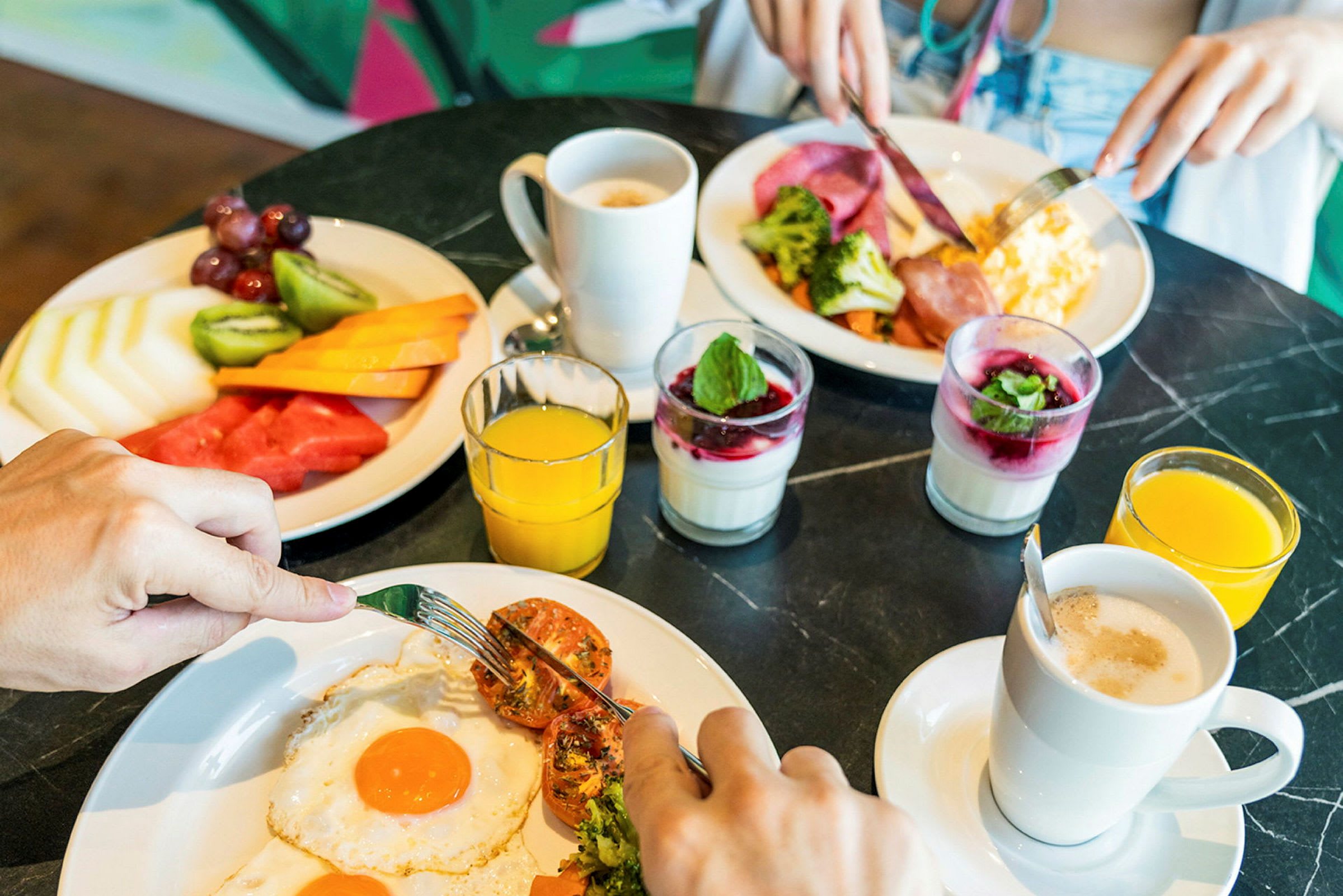 Två tallrikar med frukostmat inklusive ägg, frukt, broccoli och kalla drycker. (AI-genererad text)