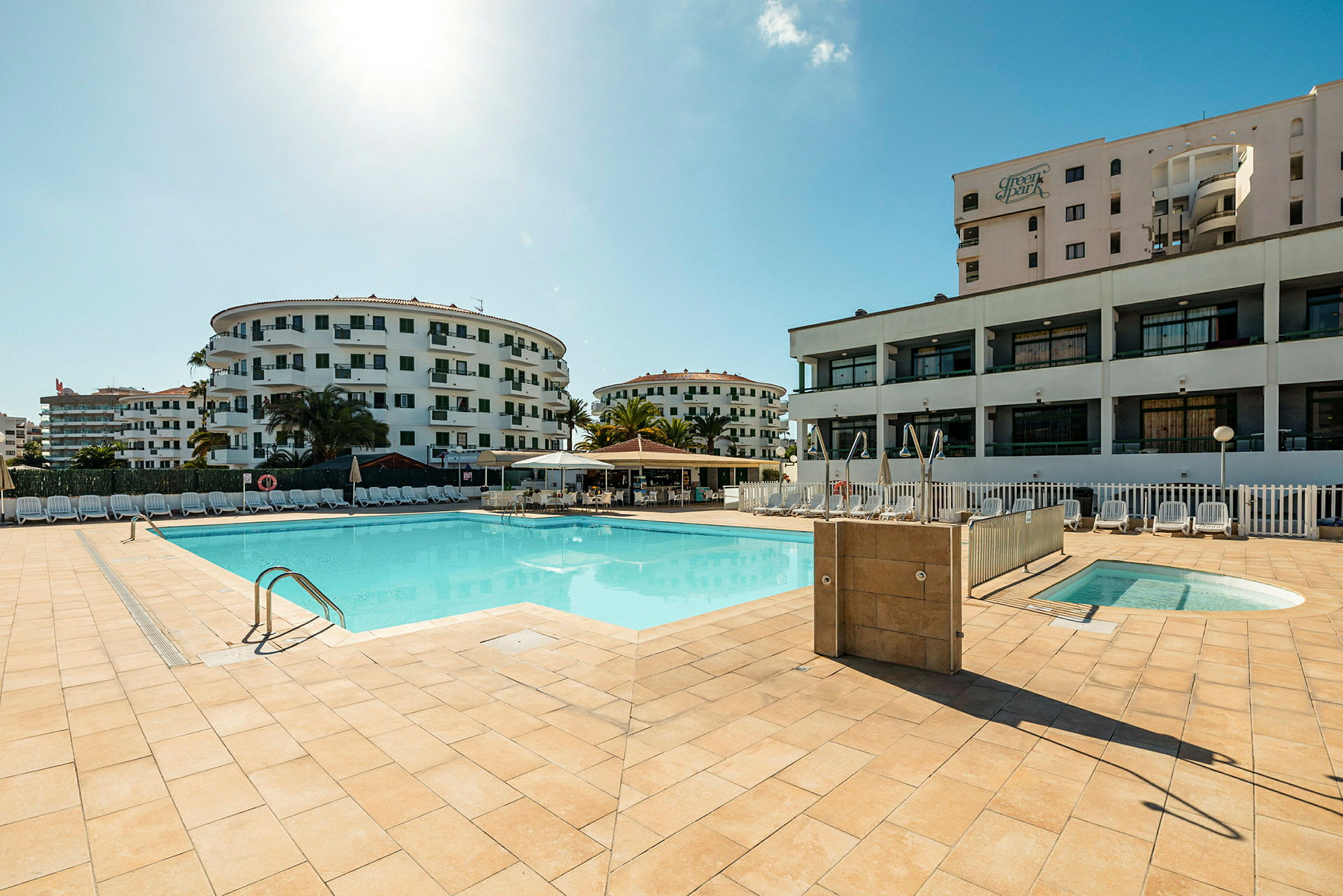En pool med omgivande hotellbyggnader och solstolar. (AI-genererad text)