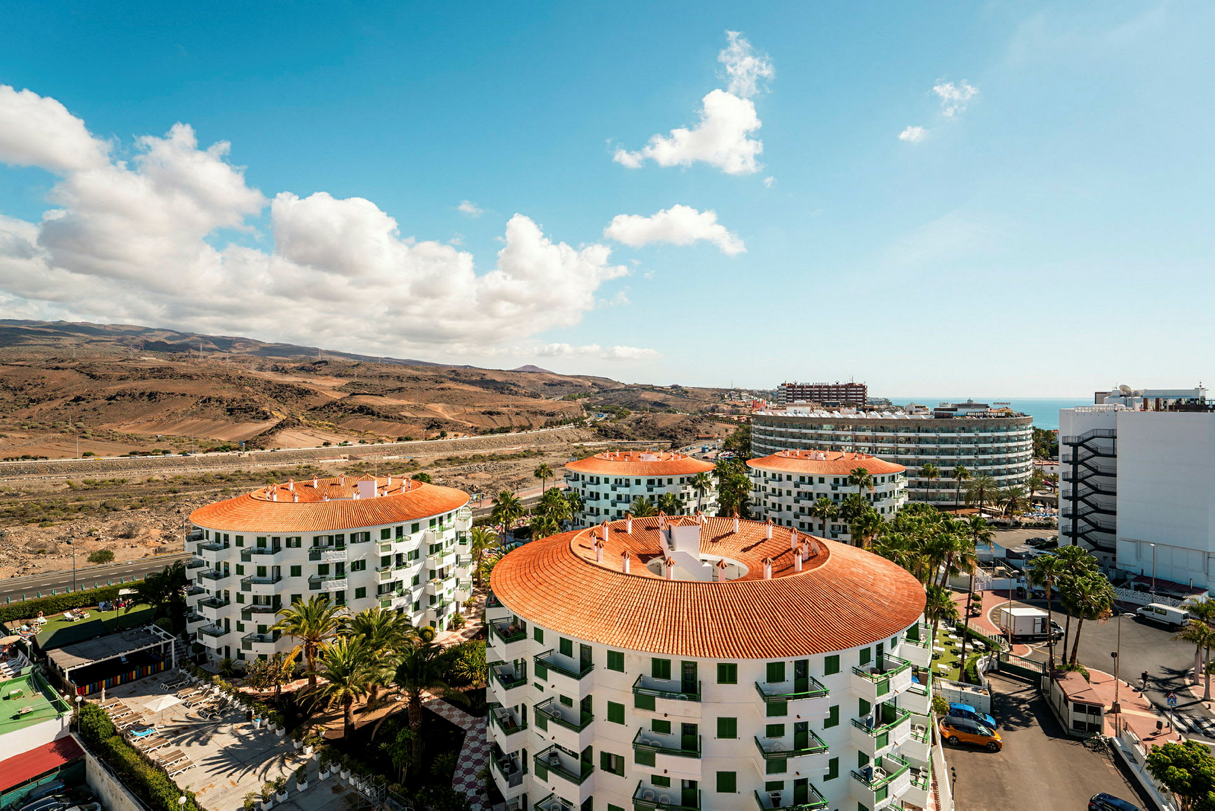 Vy över hotellbyggnader med orangea tak, landskap och hav. (AI-genererad text)
