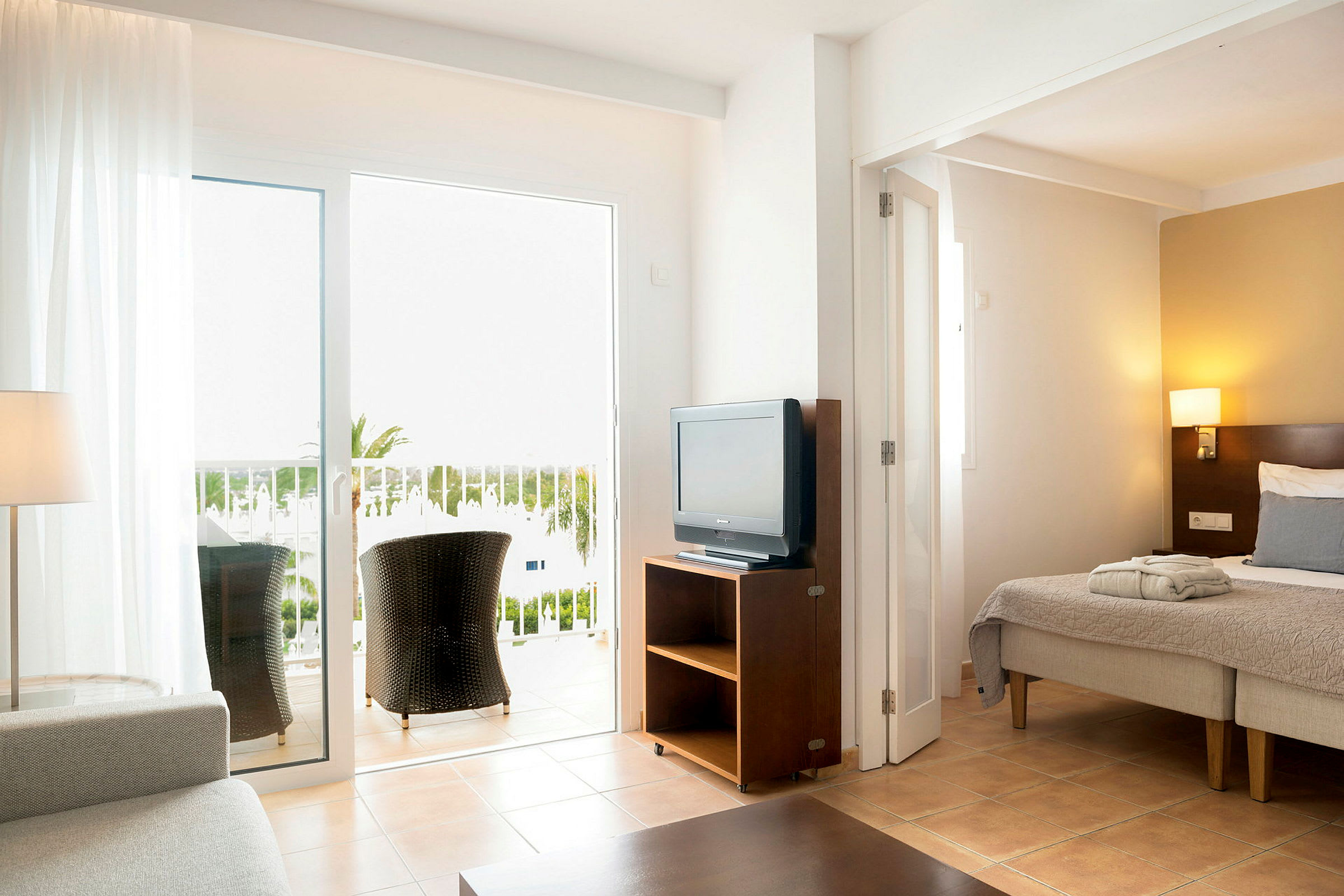 Ett hotellrum med säng, TV, och balkong med sittplatser. (AI-genererad text)