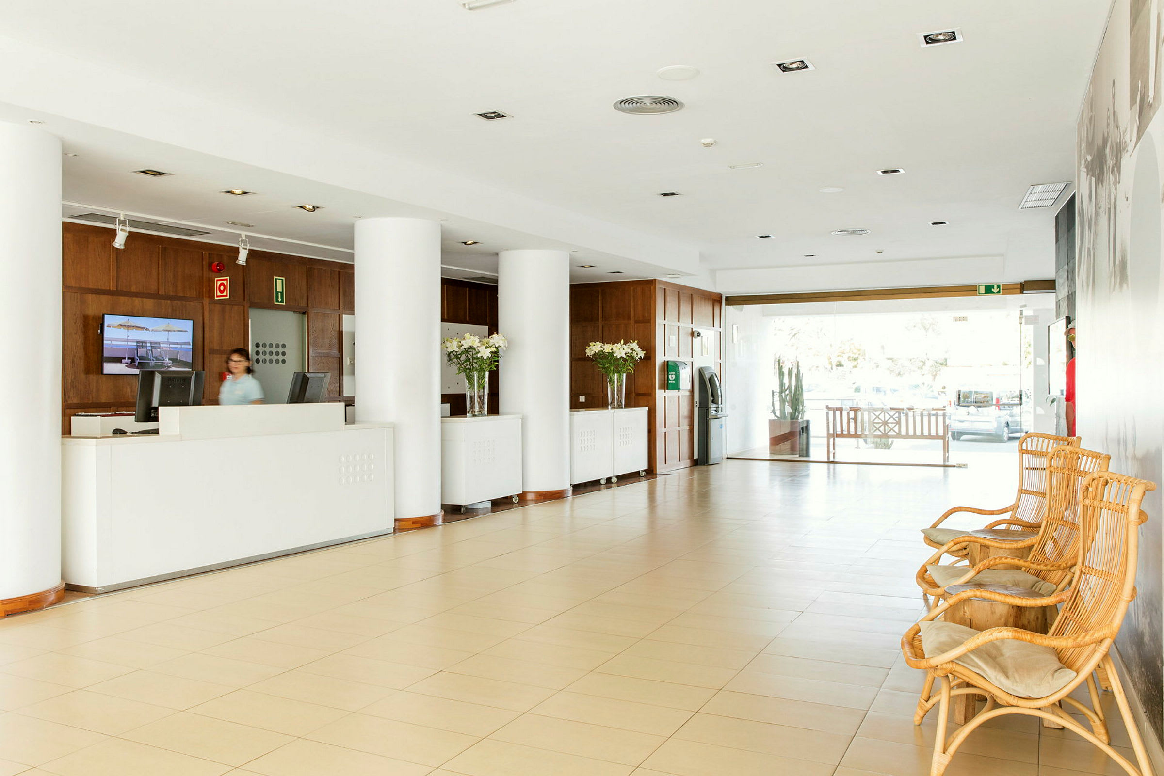 Hotellets lobby med reception, stora pelare och sittmöbler av rotting. (AI-genererad text)