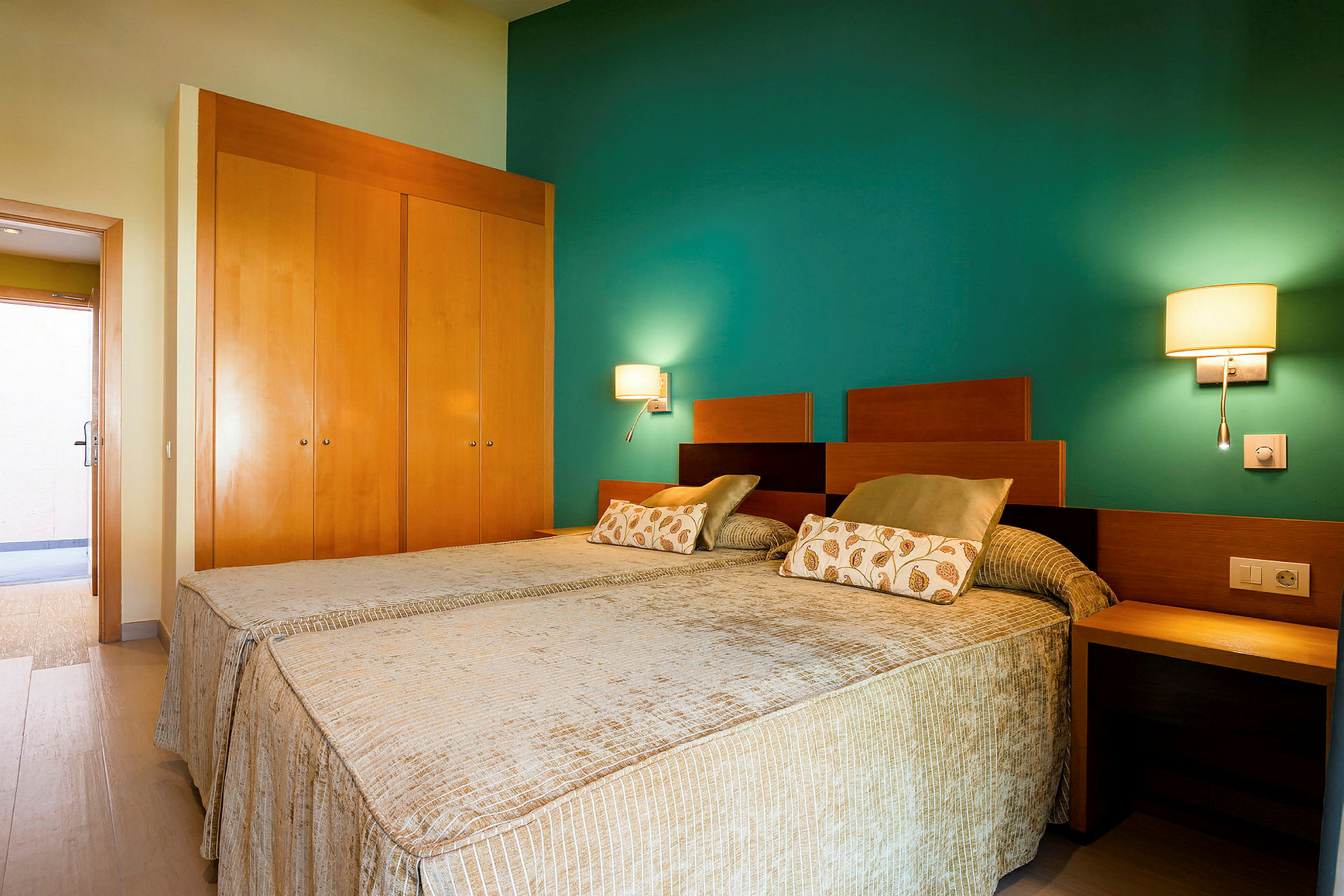 Ett hotellrum med två enkelsängar, en grön vägg och en trä garderob. (AI-genererad text)