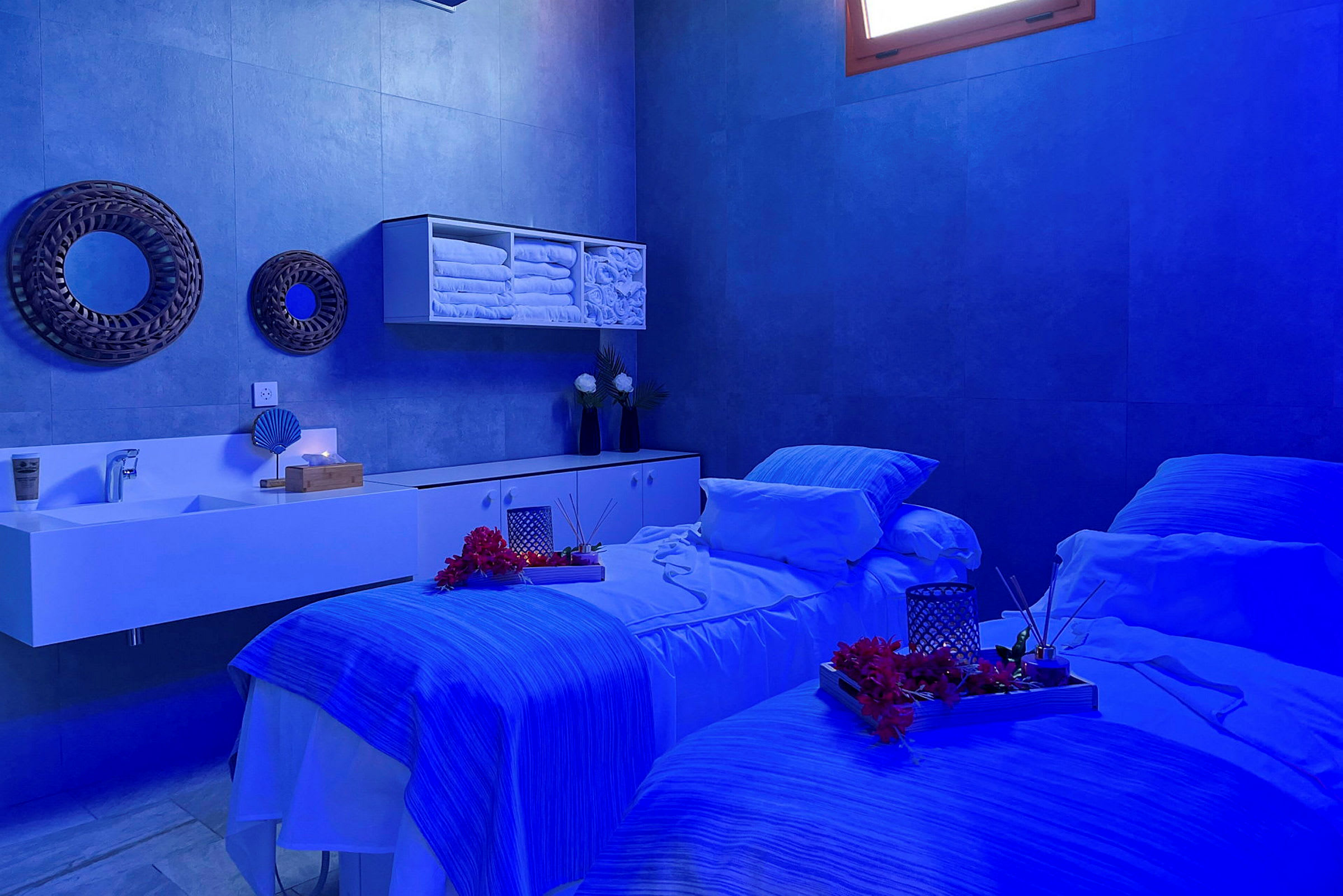 Ett spa-rum med två massagebänkar, blå belysning och dekorativa detaljer. (AI-genererad text)