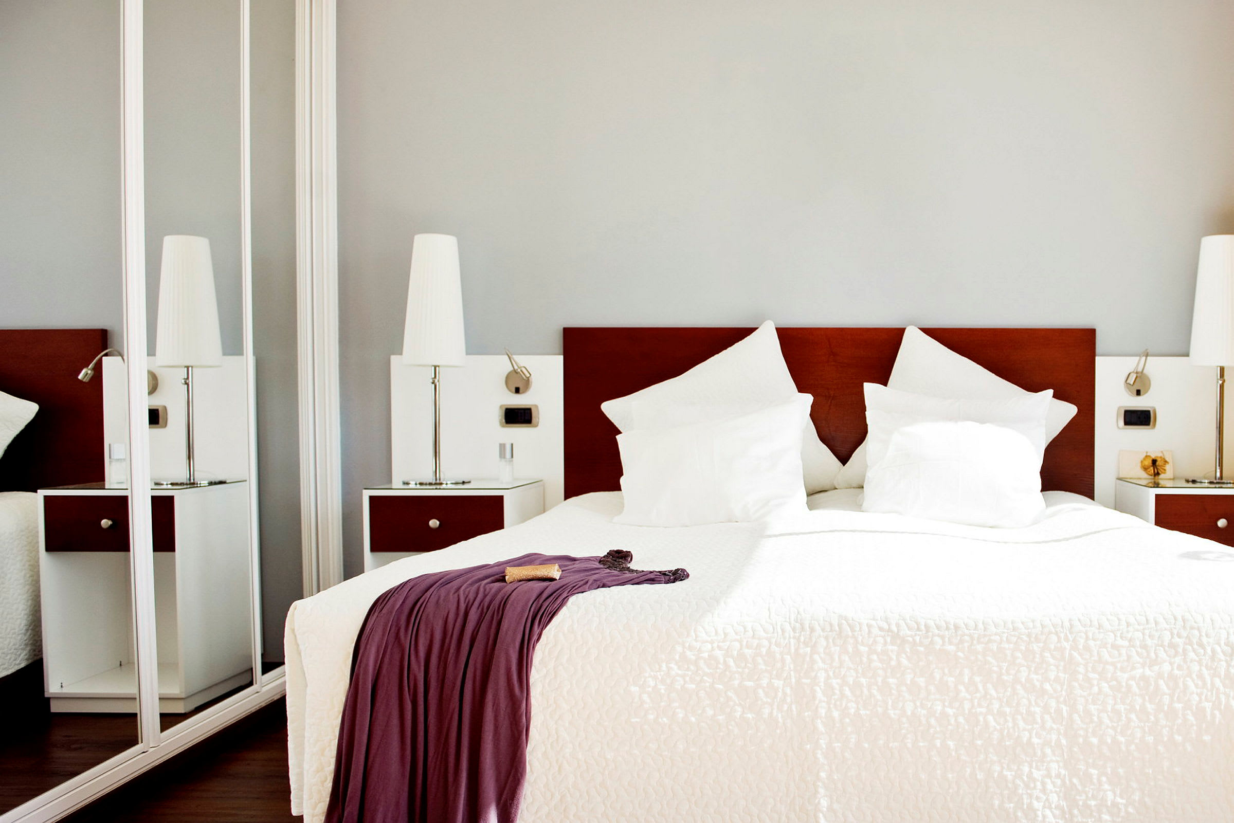Ett hotellrum med en dubbelsäng som har vita lakan och kuddar samt ett täcke med en draperad filt. (AI-genererad text)
