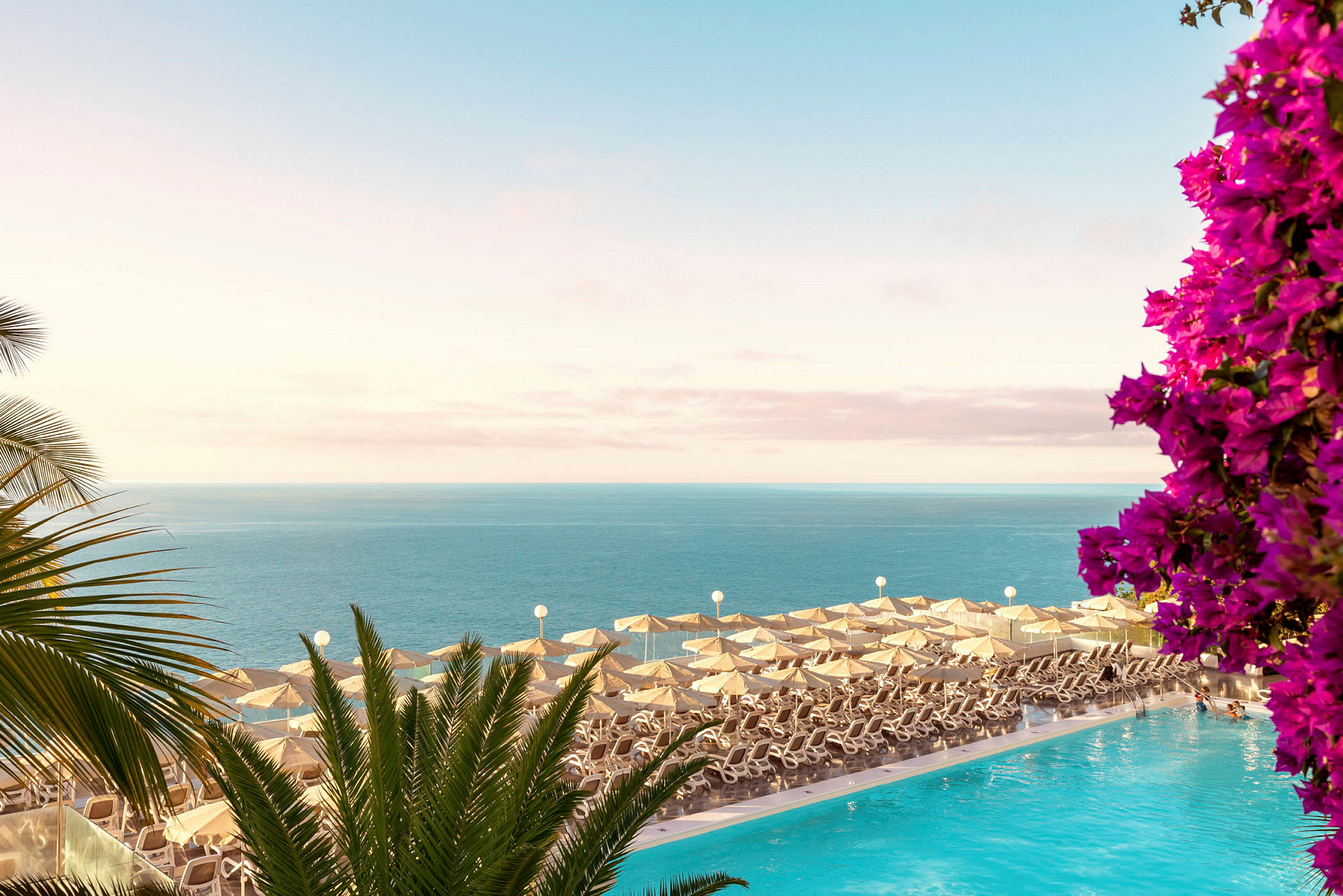 Solstolar med parasoller vid en pool med utsikt över havet och blommor. (AI-genererad text)