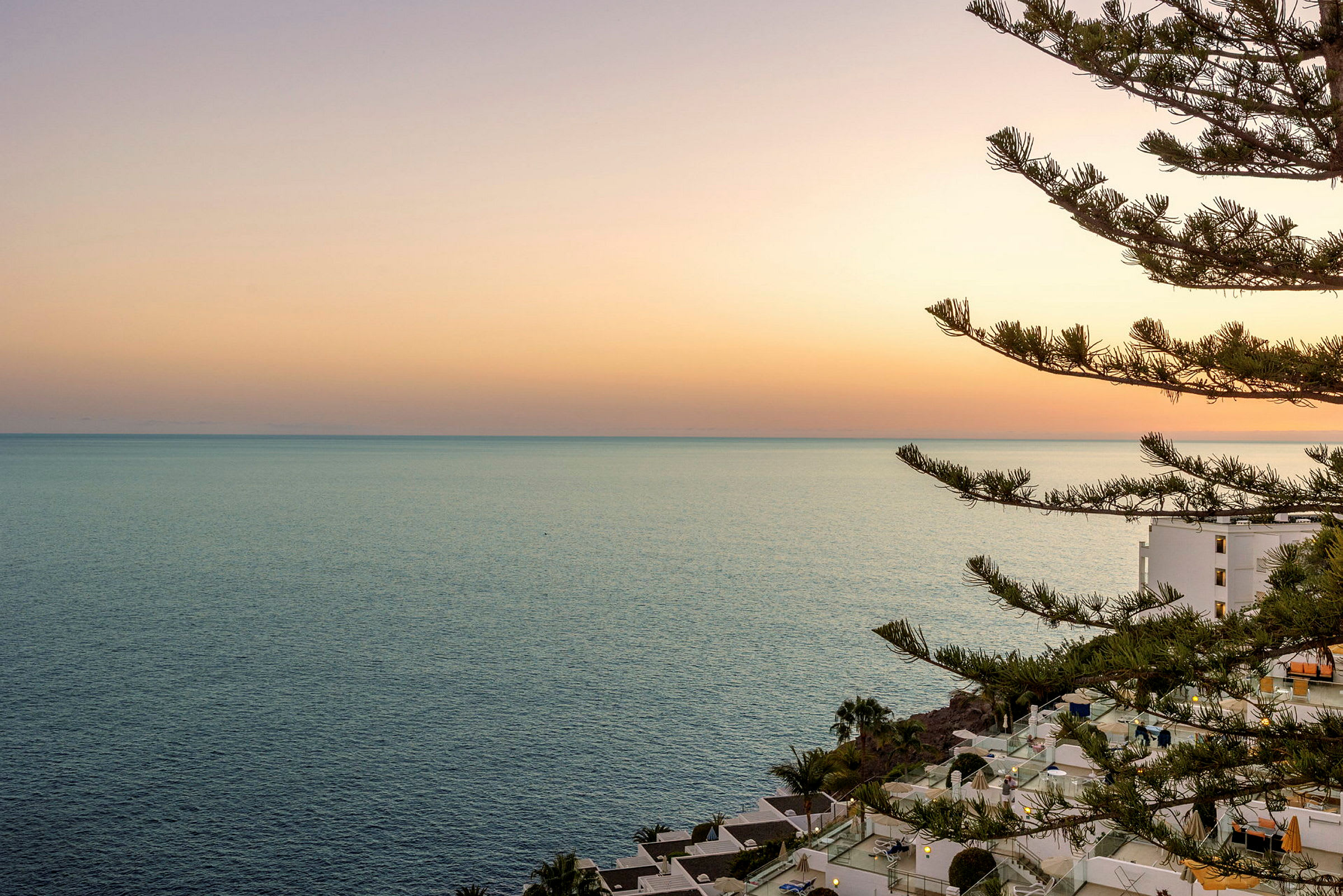 Solnedgång över havet med en byggnad och träd i förgrunden. (AI-genererad text)