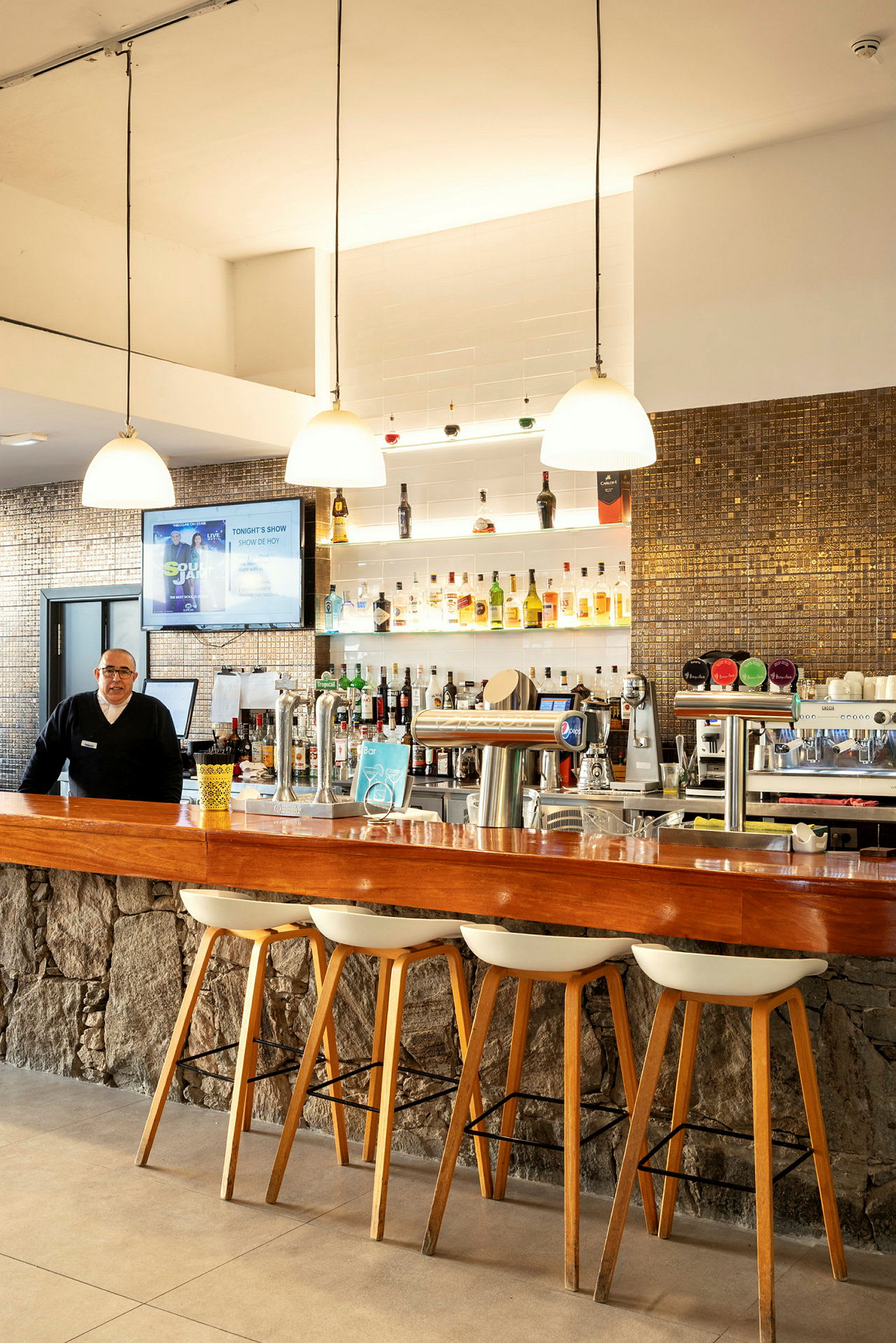 En hotellbar med trädisk och stolar, samt hyllor fyllda med flaskor. (AI-genererad text)