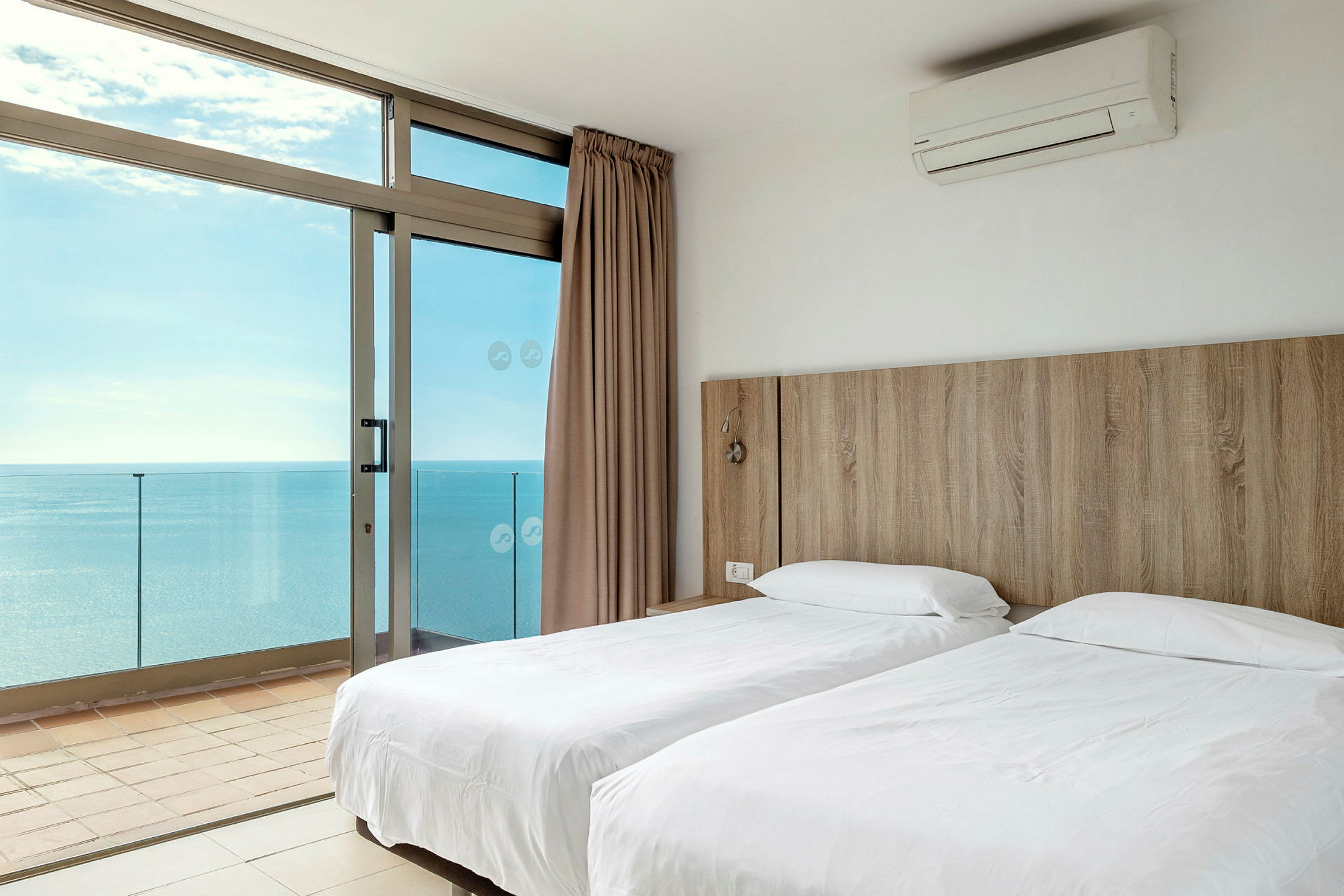 Ett hotellrum med två enkelsängar och utsikt över havet genom stora fönster. (AI-genererad text)