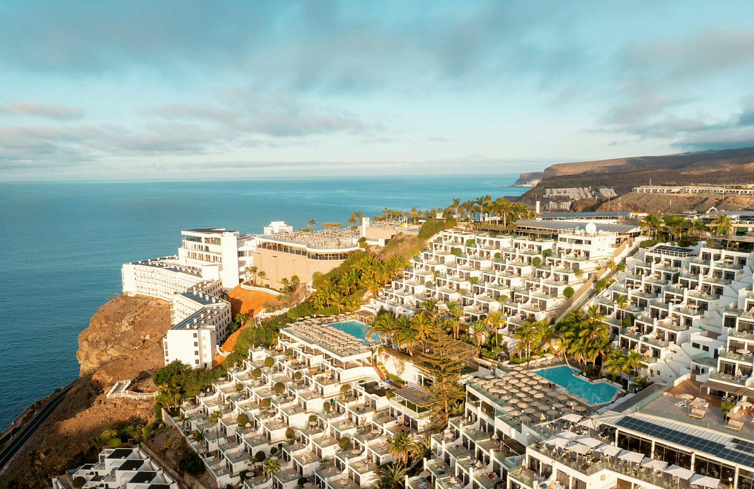 Hotellkomplex på en klippa med pooler och havsutsikt. (AI-genererad text)