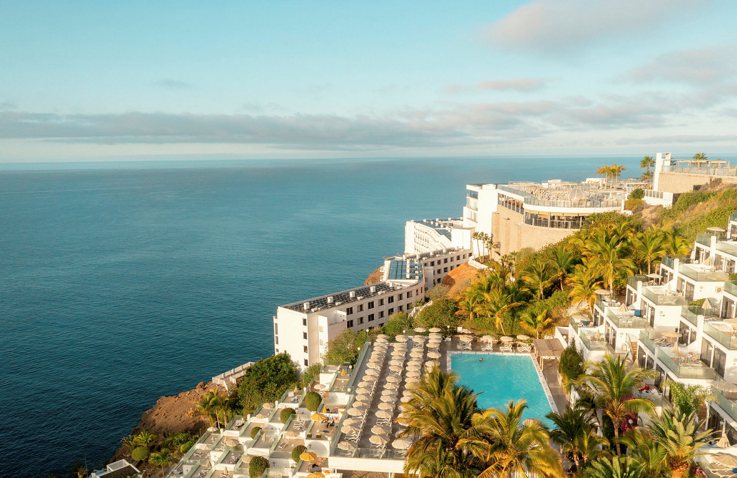 Utsikt mot havet med ett hotellkomplex och pool omgivna av grönska. (AI-genererad text)
