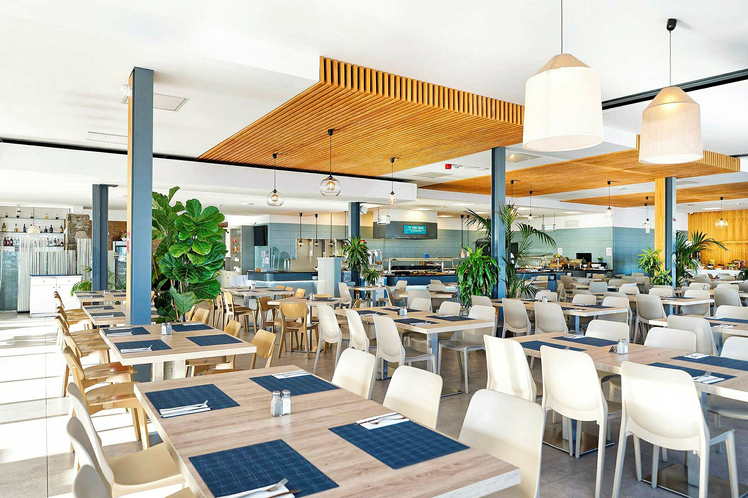 En restaurang med moderna möbler samt bord och stolar. Dekorationer inkluderar stora krukväxter. (AI-genererad text)