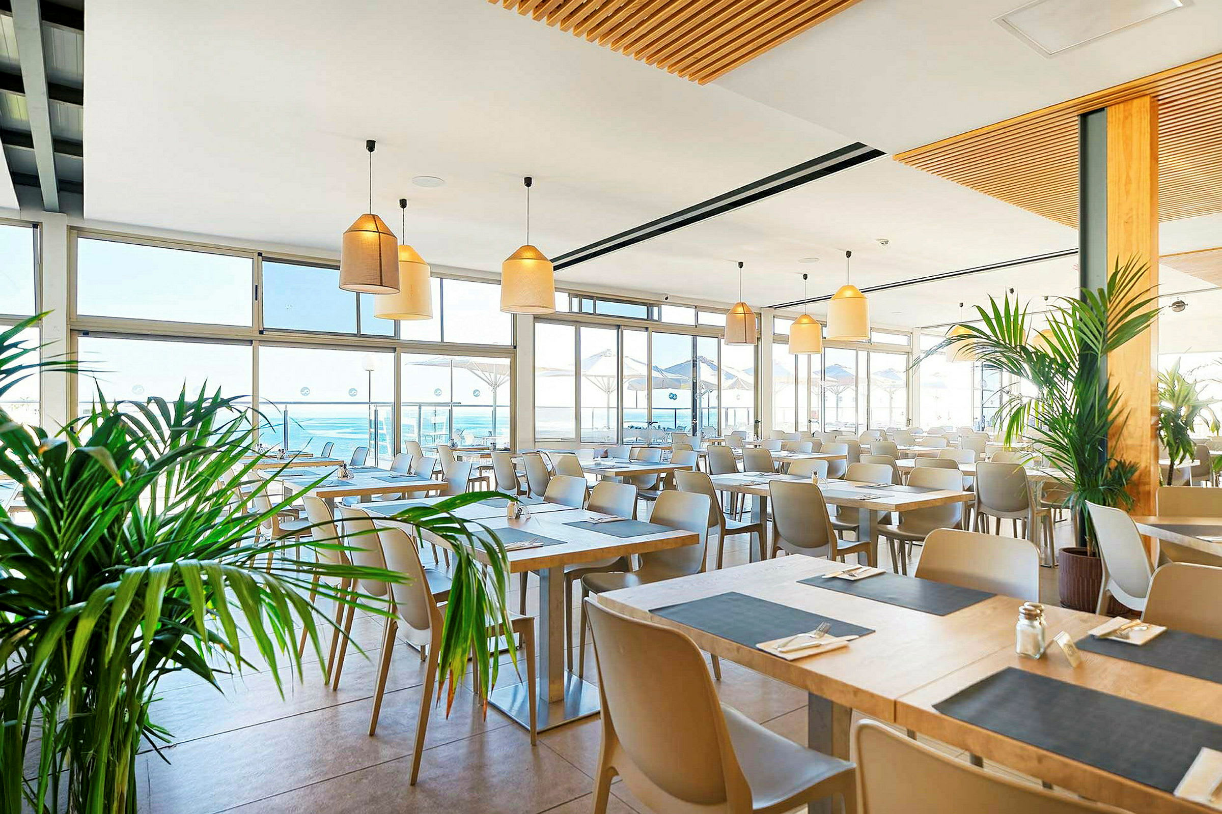 Ljus och modern restaurang med många bord, stora fönster och växter. (AI-genererad text)