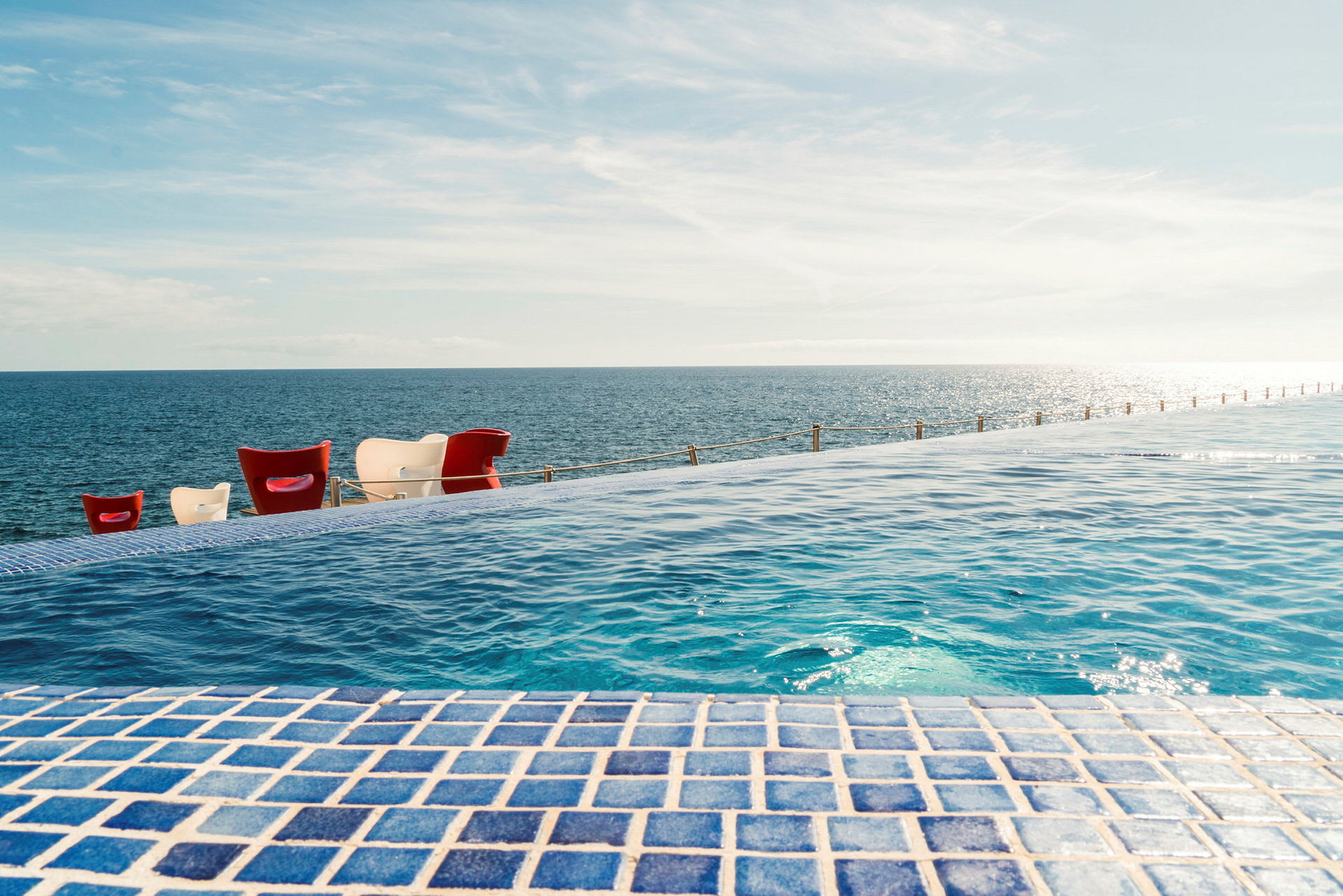 Utsikt över en infinitypool med blå mosaik som sträcker sig mot havet och himlen. (AI-genererad text)