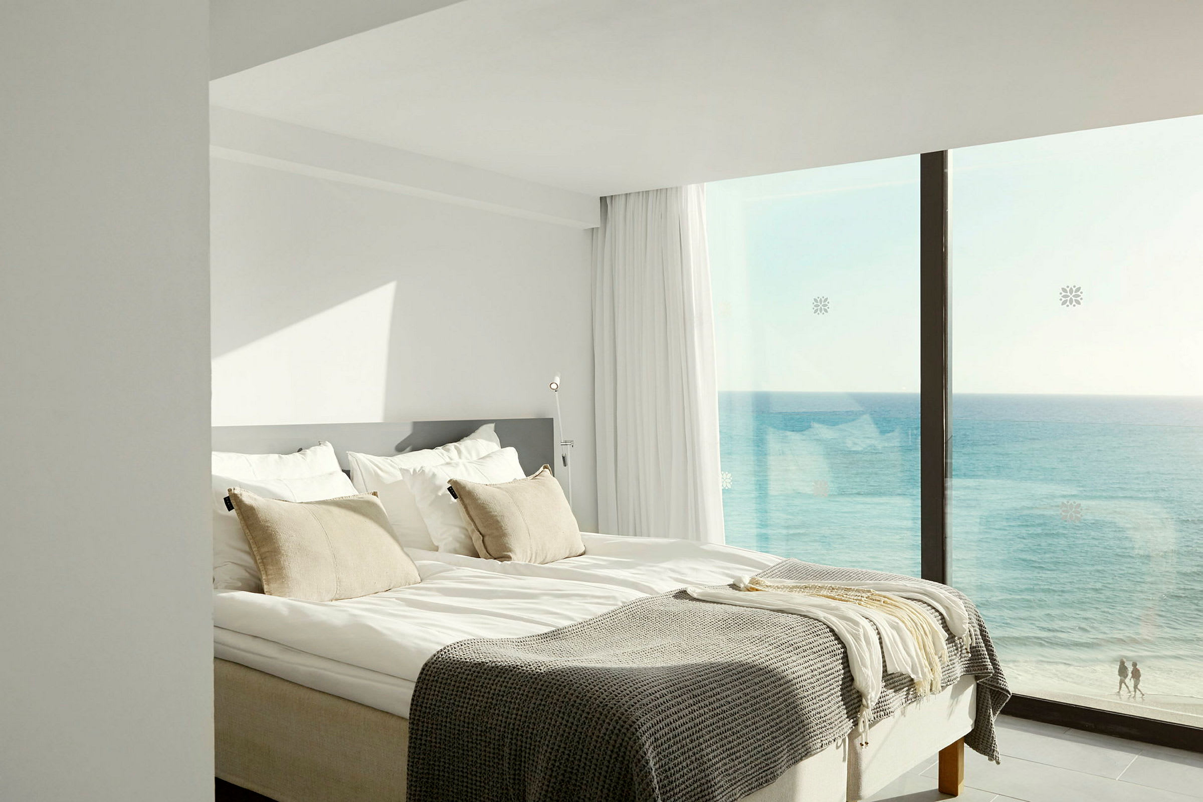 Ett ljust och luftigt hotellrum med en dubbelsäng, stora fönster och havsutsikt. (AI-genererad text)
