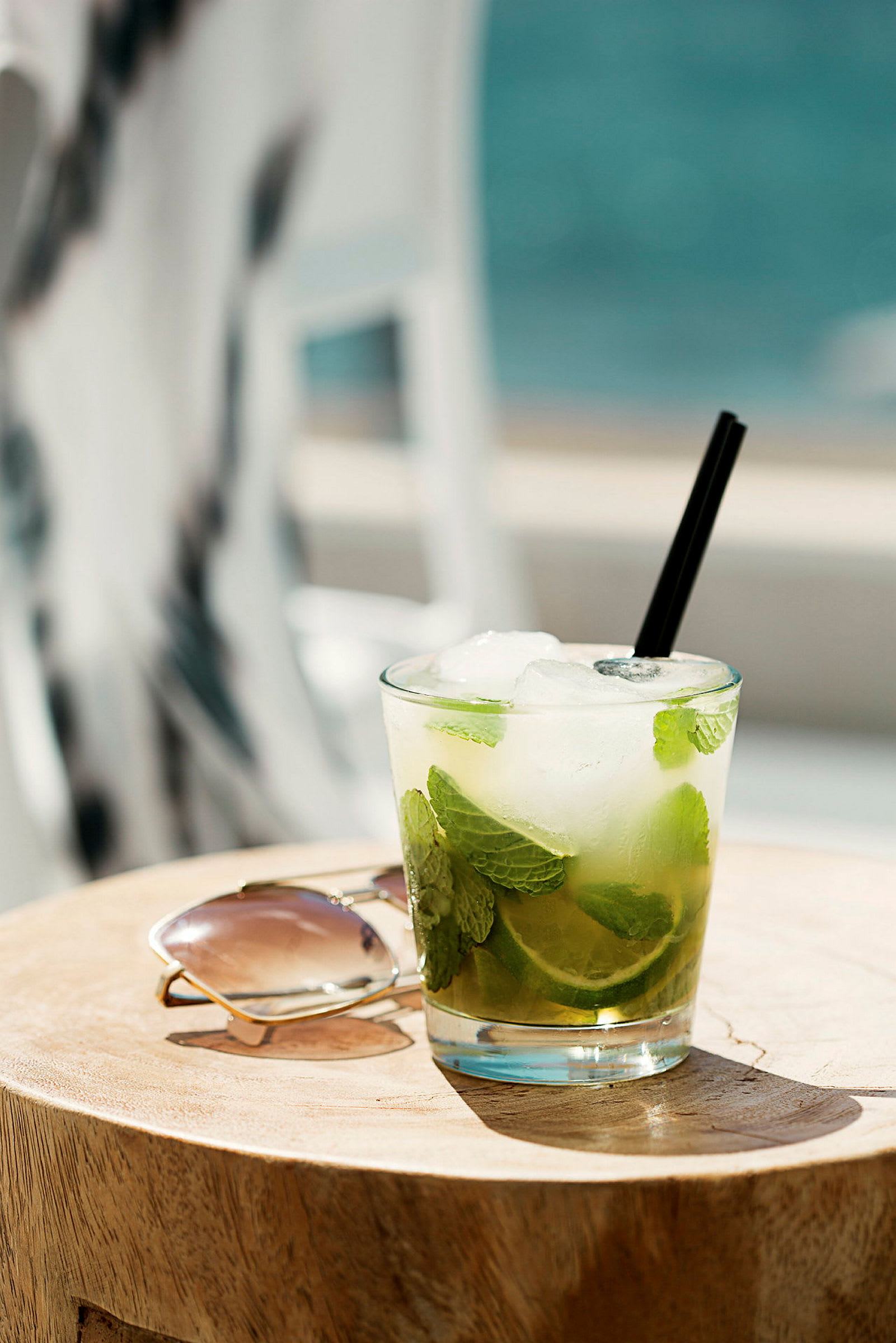 Ett glas med lime och mynta bredvid ett par solglasögon på ett träbord. (AI-genererad text)