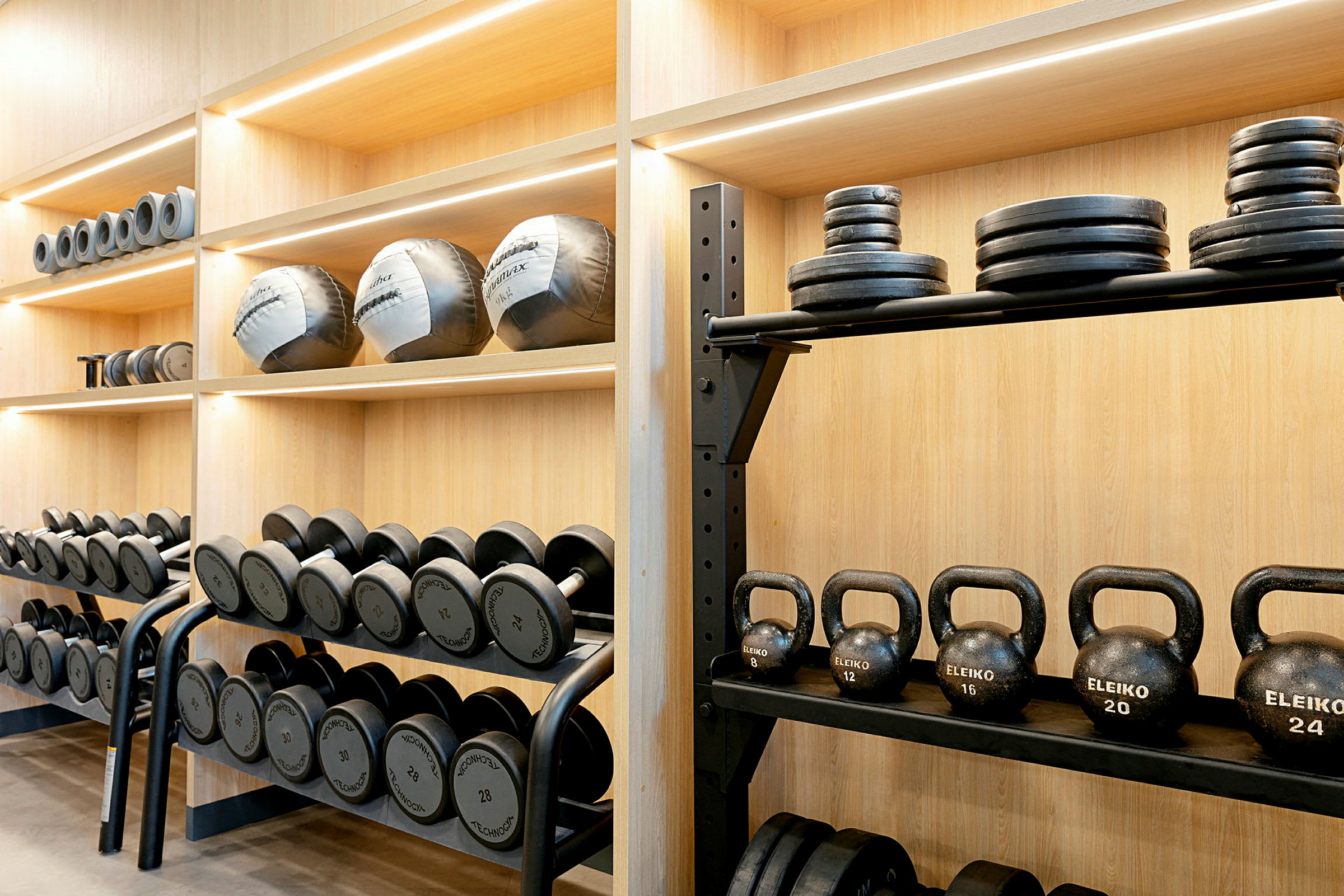 Hylla med olika träningsredskap såsom hantlar, kettlebells och viktskivor. (AI-genererad text)
