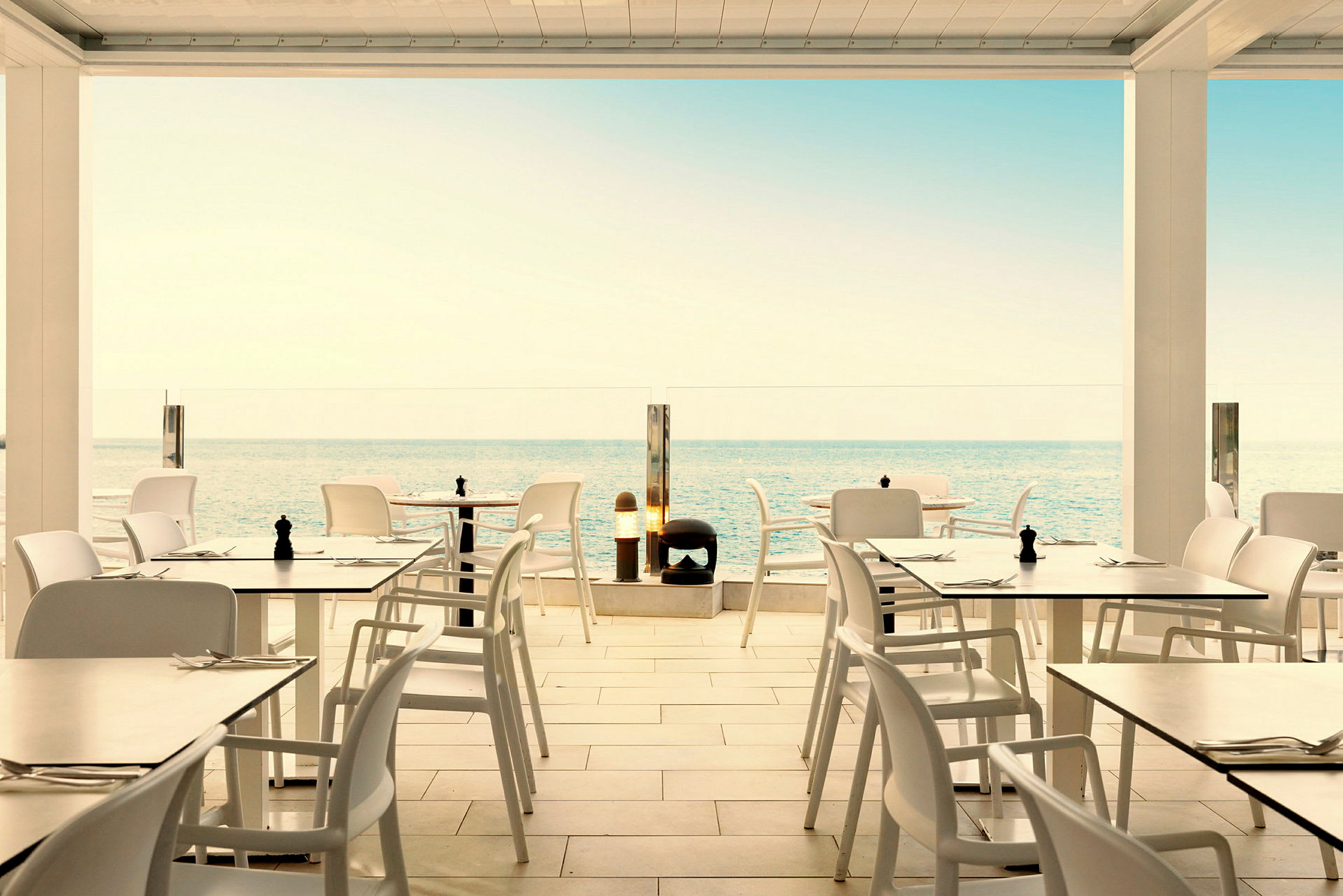 Restaurang med vita bord och stolar med utsikt över havet. (AI-genererad text)