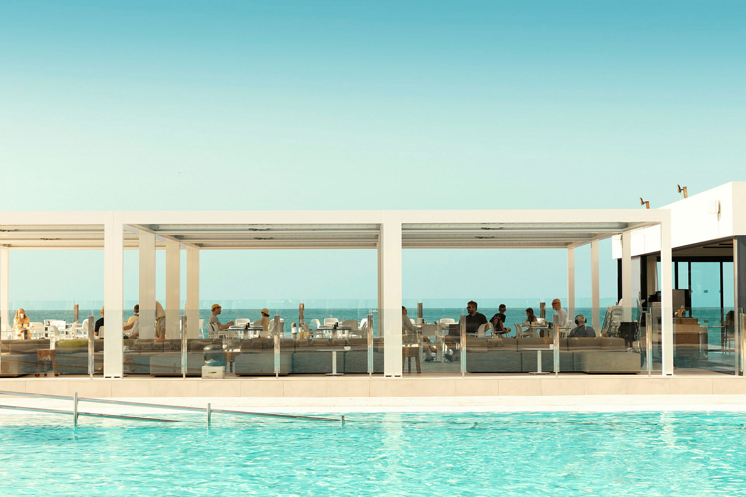 Utomhusterrass med sittplatser vid en pool och hav i bakgrunden. (AI-genererad text)