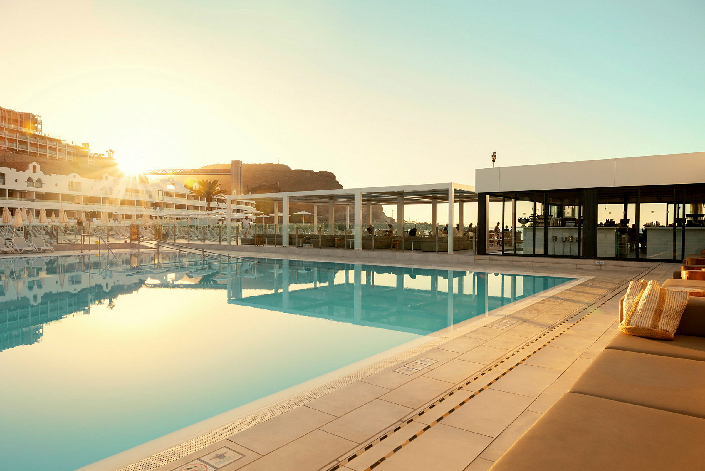 Utomhuspool vid ett hotell med solstolar och en byggnad i bakgrunden. (AI-genererad text)