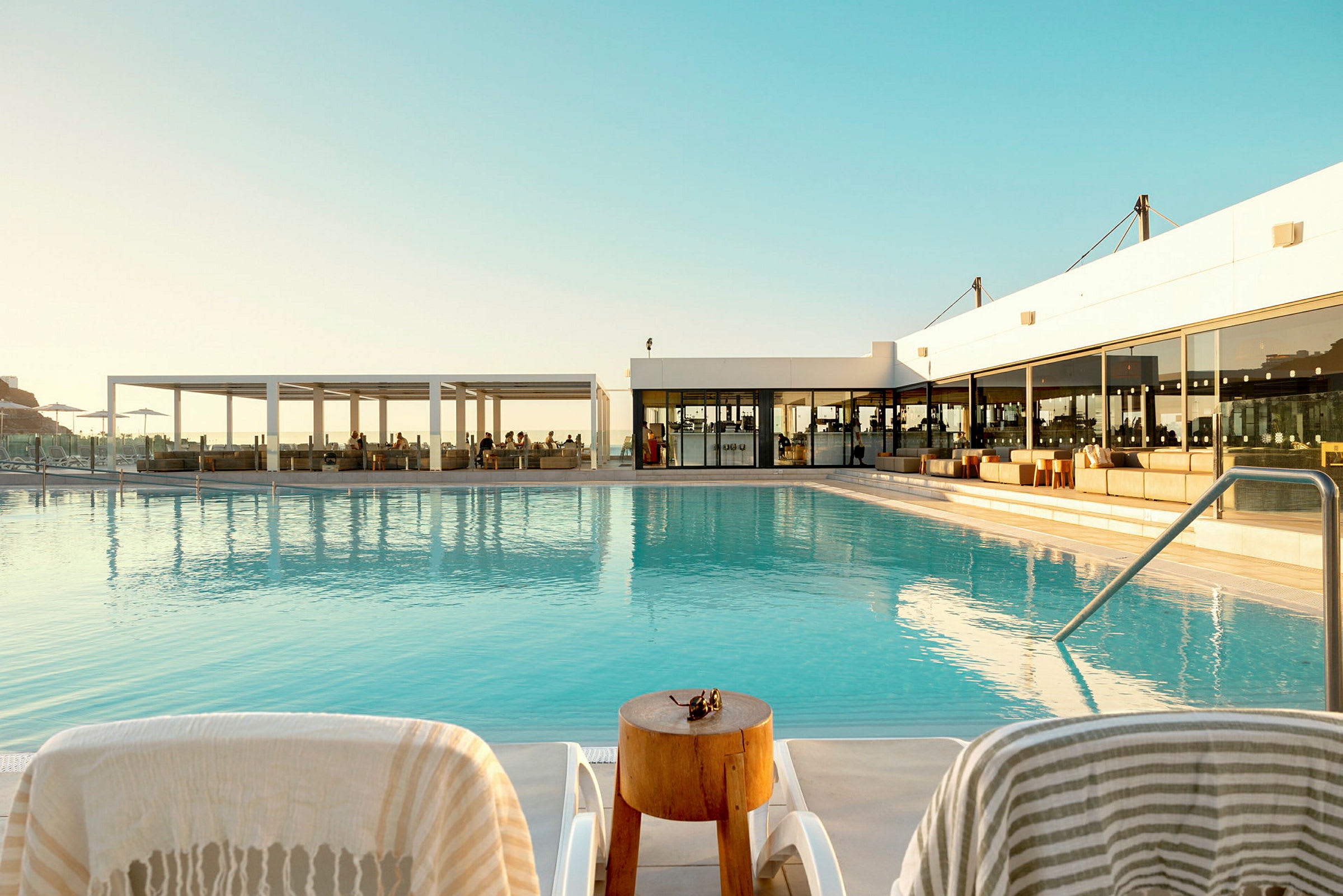 Poolområde med solstolar och utsikt mot restaurangbyggnad. (AI-genererad text)