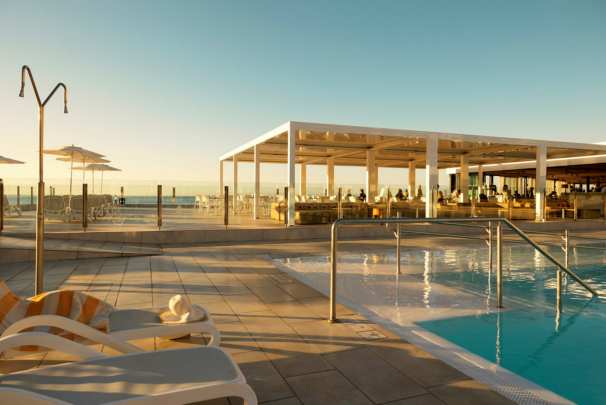 Soluppgång över en pool med vilstolar och restaurangområde. (AI-genererad text)