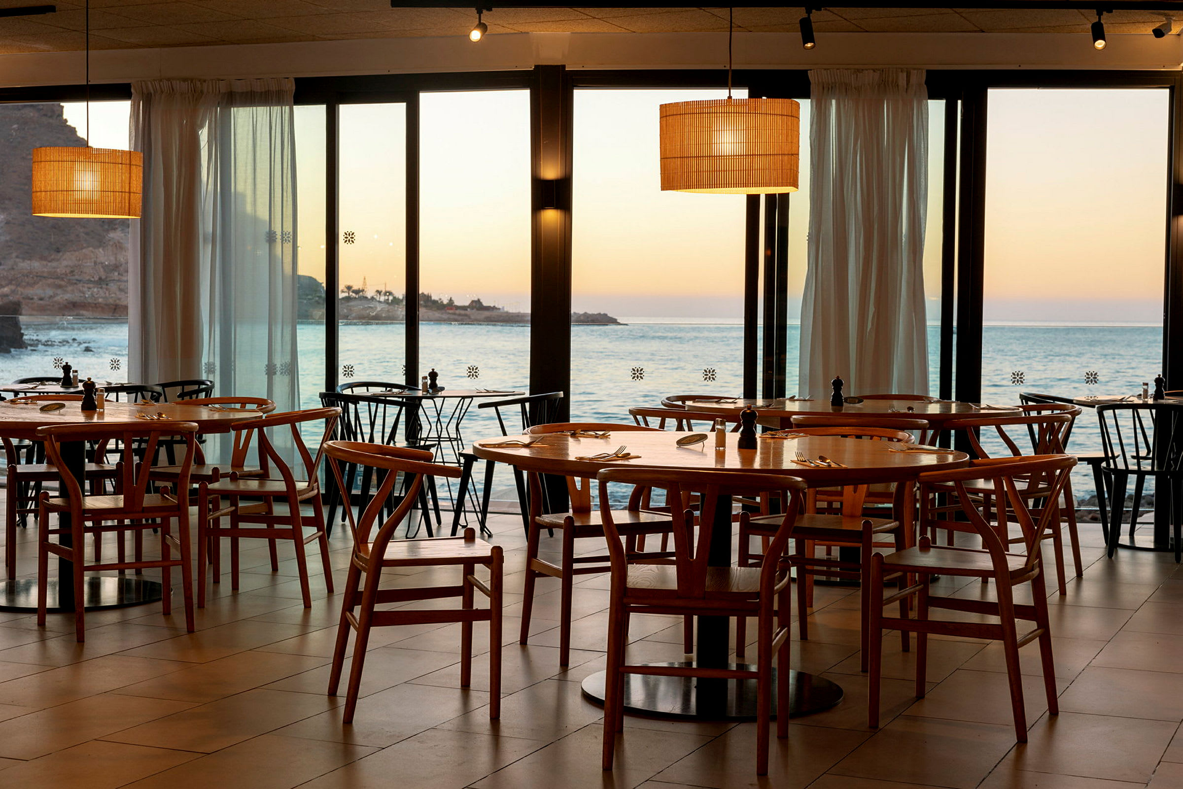 Restaurang med trästolar och bord med utsikt över havet och solnedgång. (AI-genererad text)