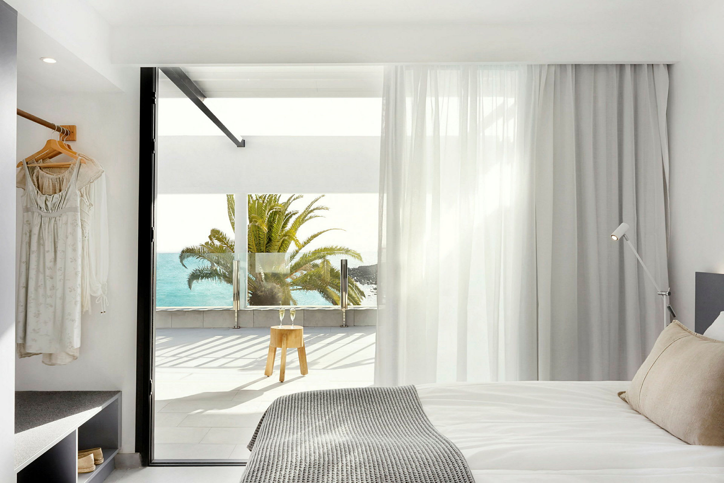 Modernt hotellrum med utsikt mot havet och en palm utanför fönstret. (AI-genererad text)