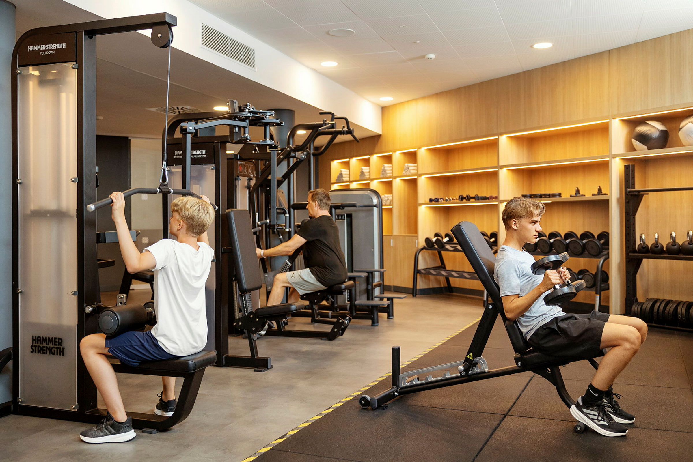 Personer som tränar i ett gym med olika träningsmaskiner och vikter. (AI-genererad text)
