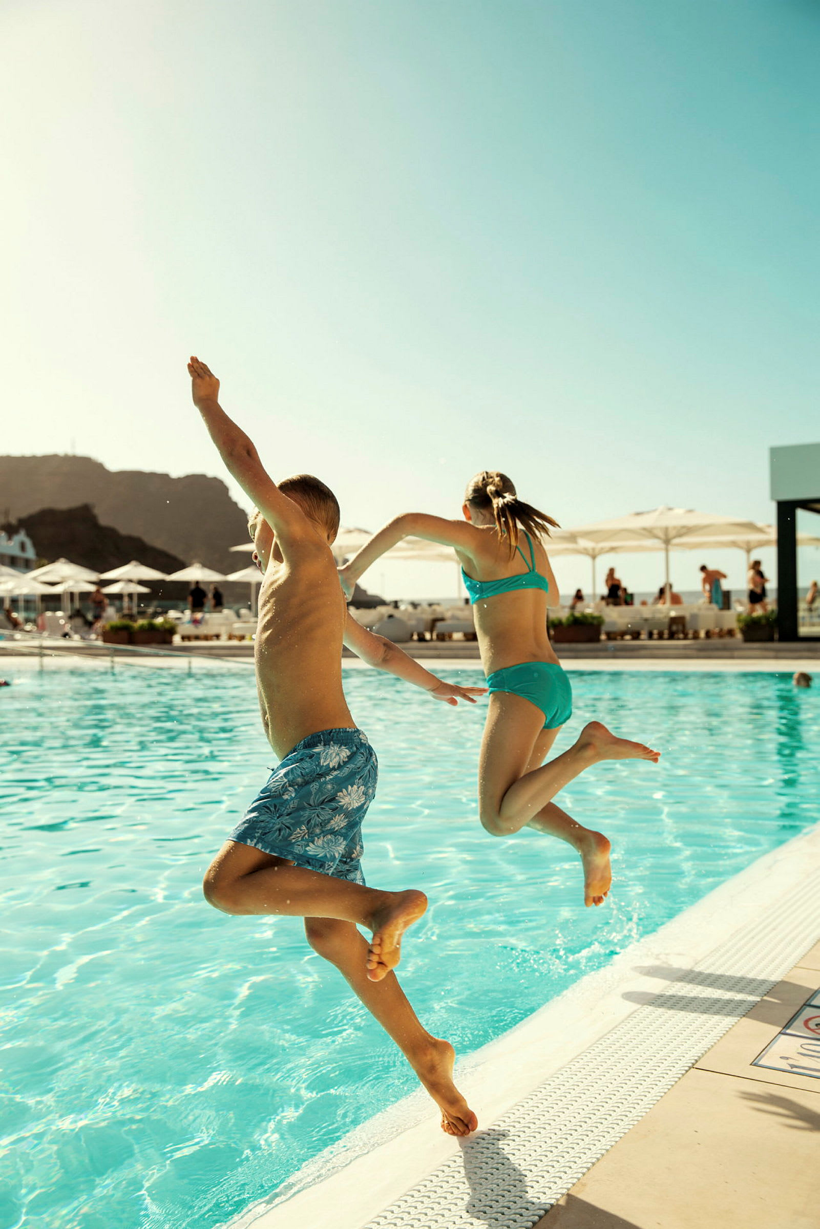 Två barn hoppar från poolkanten i en utomhuspool. (AI-genererad text)