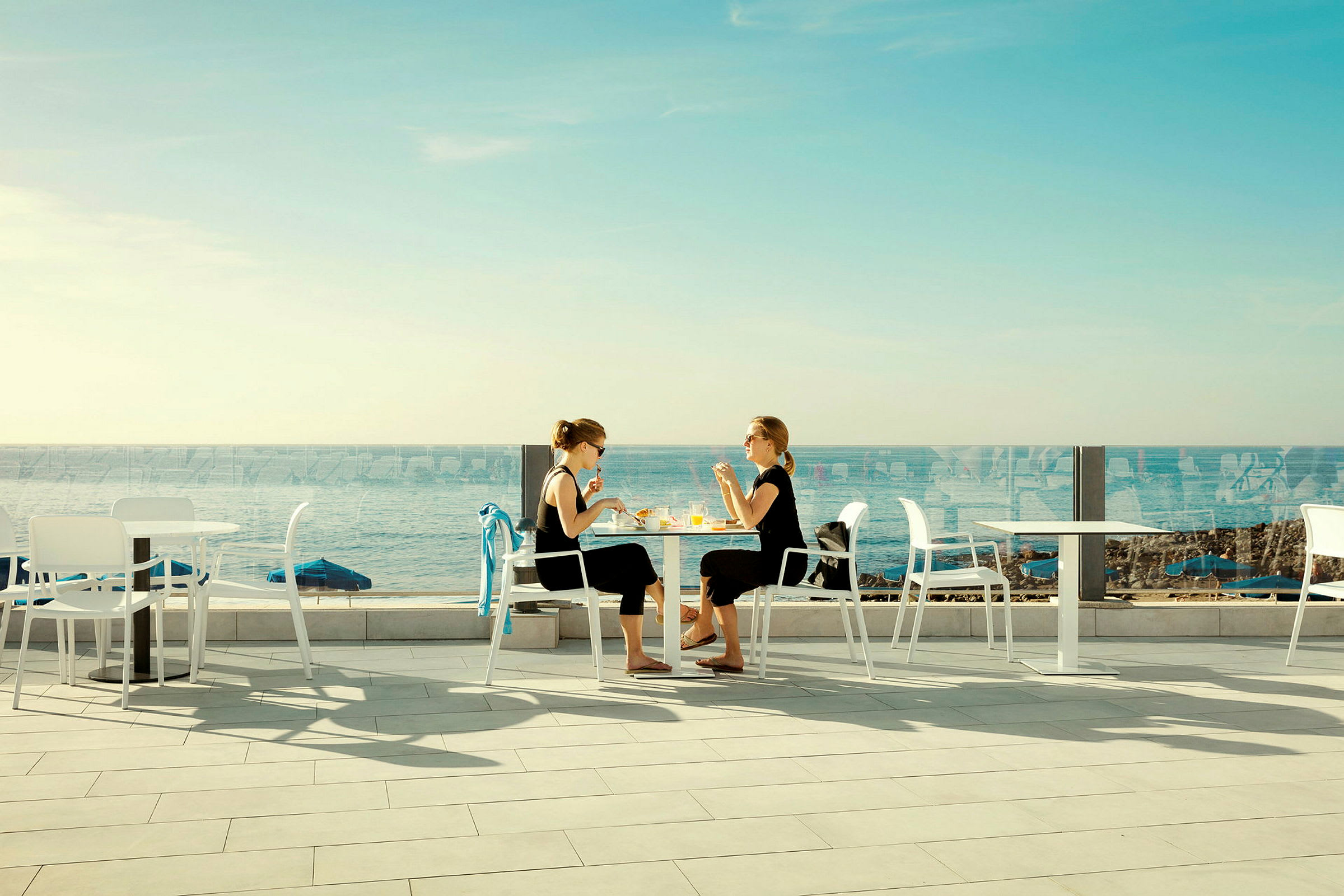 Två personer sitter vid ett bord utomhus nära havet. (AI-genererad text)