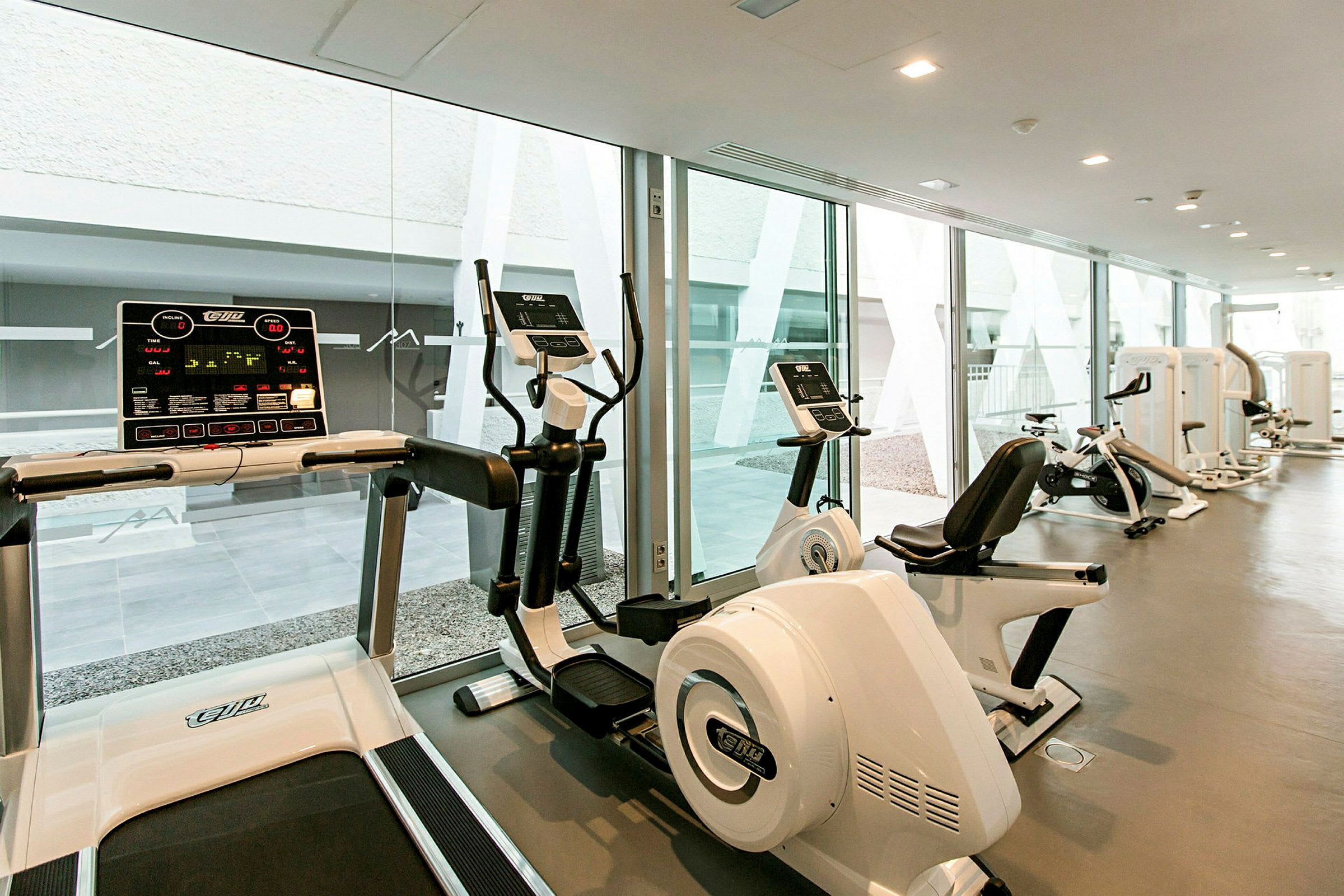 Ett gym med moderna konditionsmaskiner och stora glasfönster. (AI-genererad text)