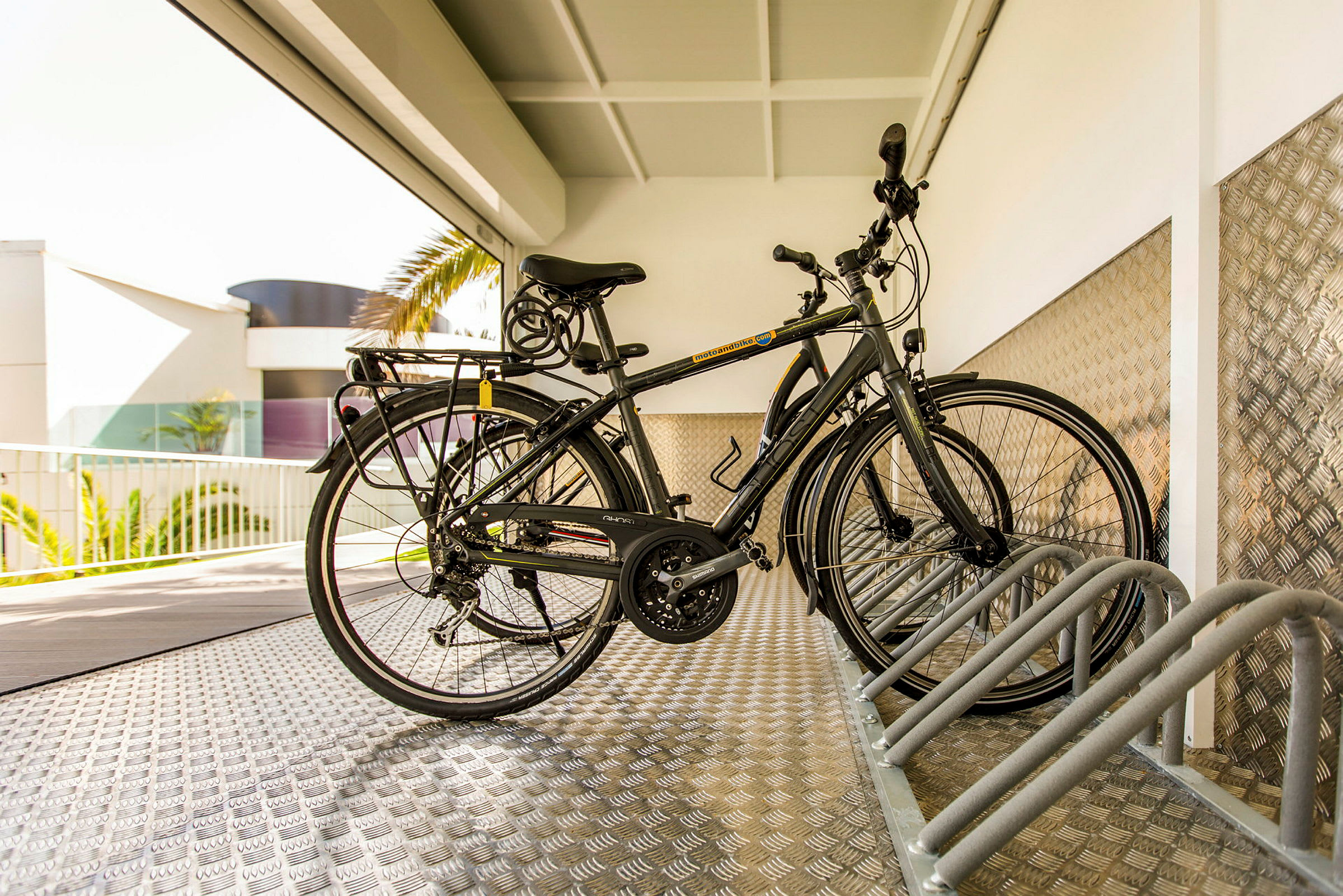 Två cyklar står parkerade i en cykelställning under ett tak. (AI-genererad text)