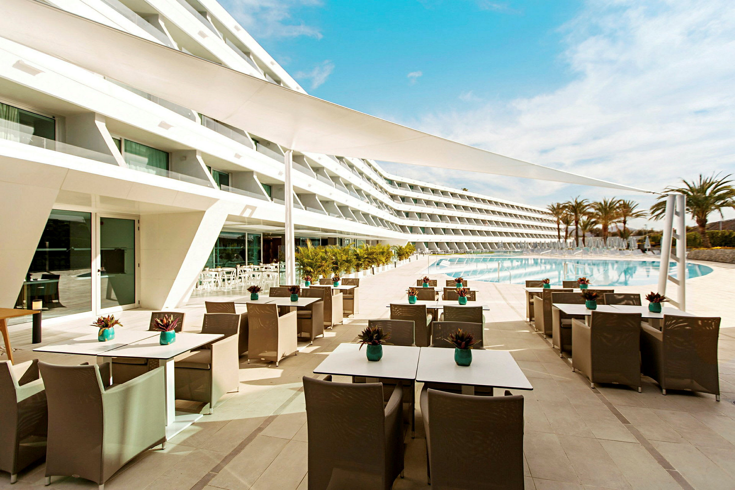 Hotellbyggnad vid en stor pool med uteservering. (AI-genererad text)