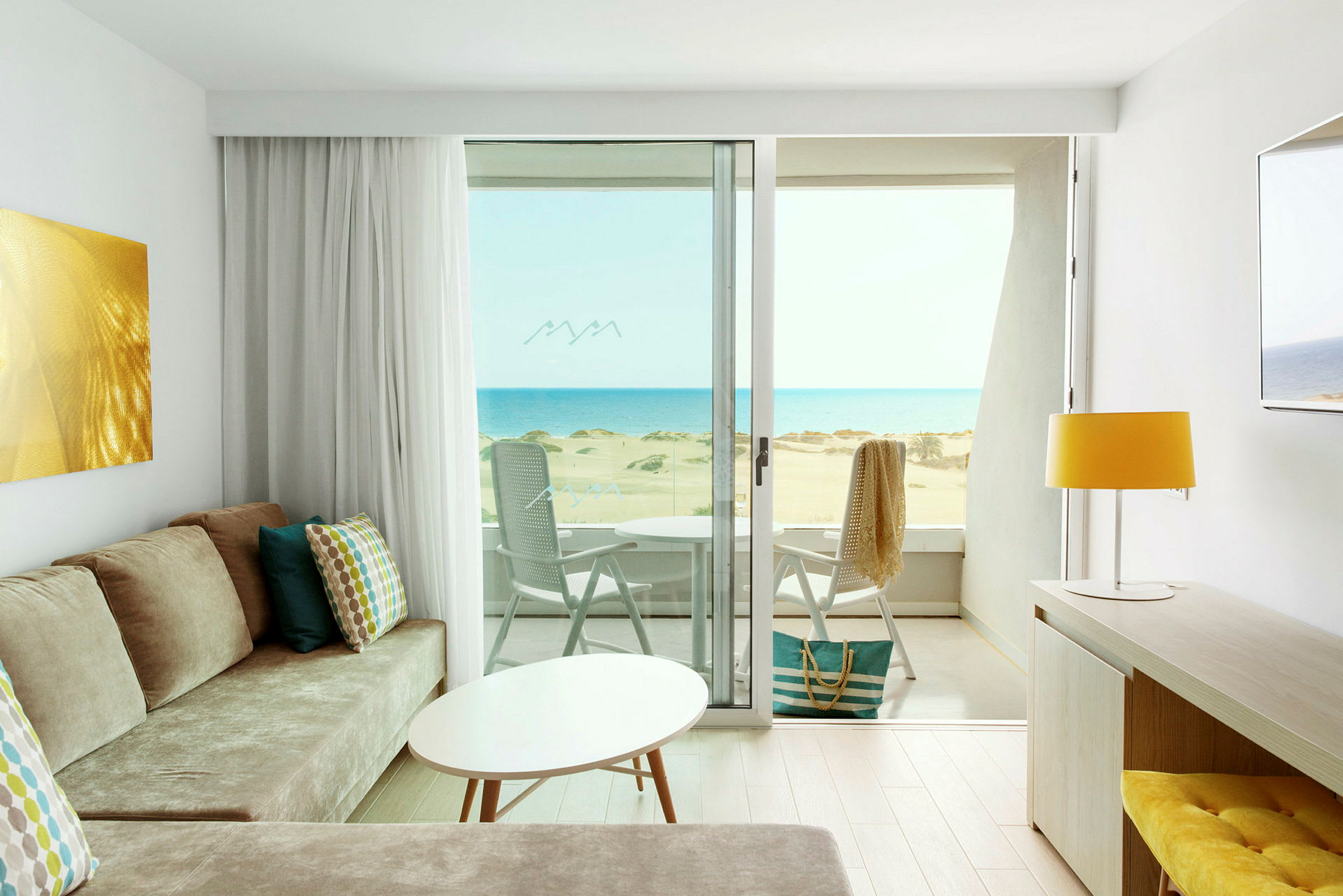 Utsikt från ett ljust hotellrum med modern inredning över en solig strand och havet. (AI-genererad text)
