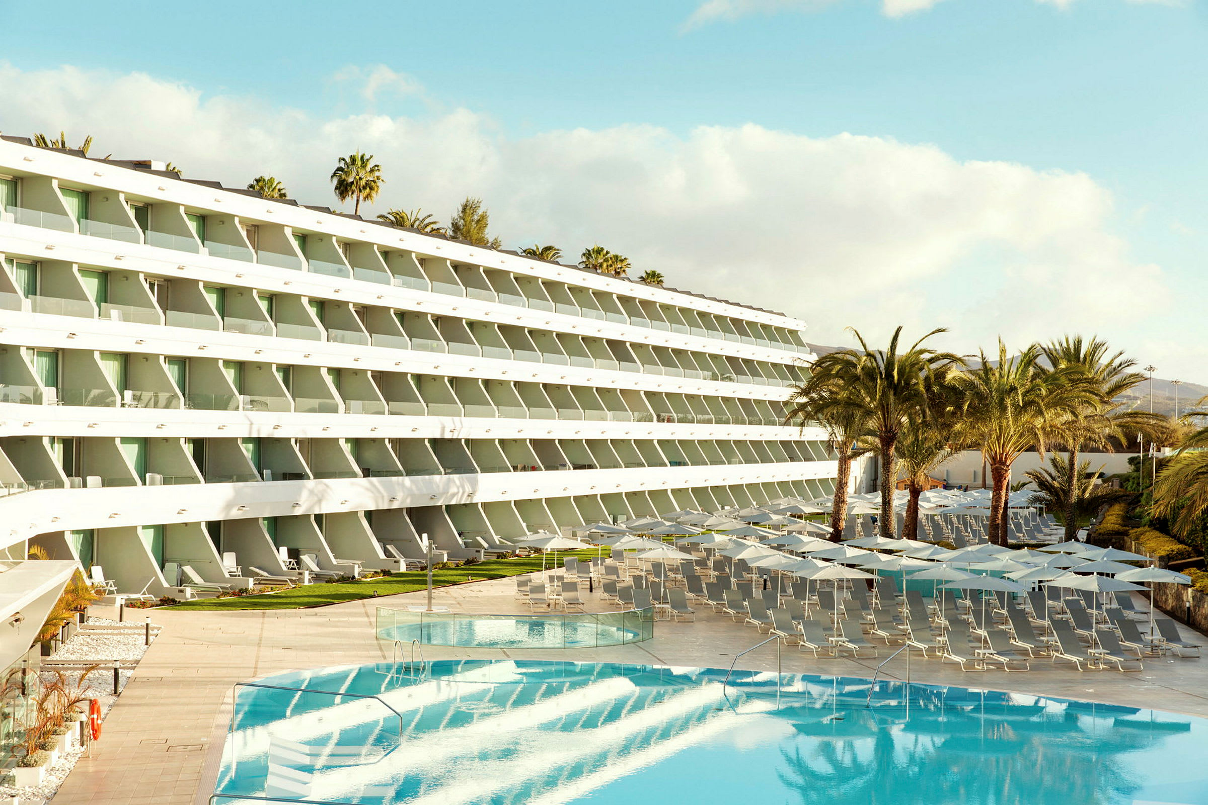 Hotellanläggning med pool, solstolar och parasoller, omgiven av palmer. (AI-genererad text)