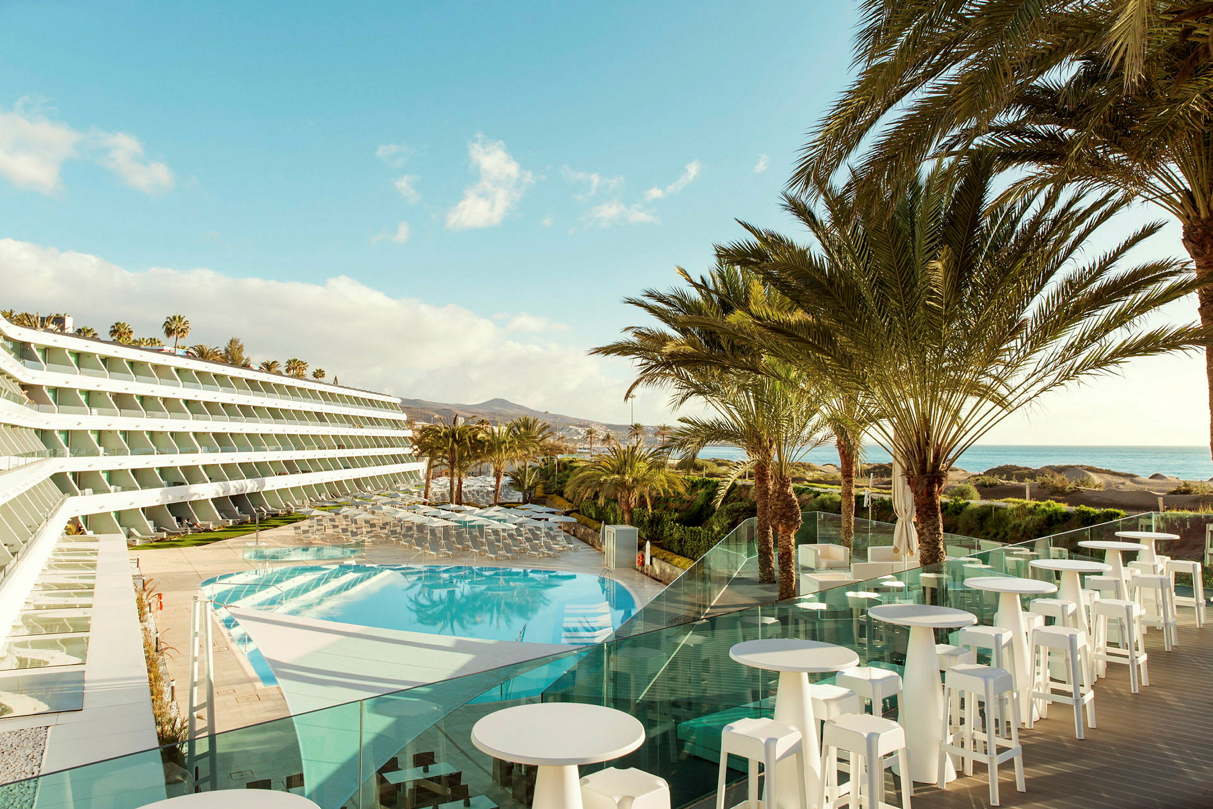 Bild av ett hotell med utsikt över en pool och palmer, med havet i bakgrunden. (AI-genererad text)
