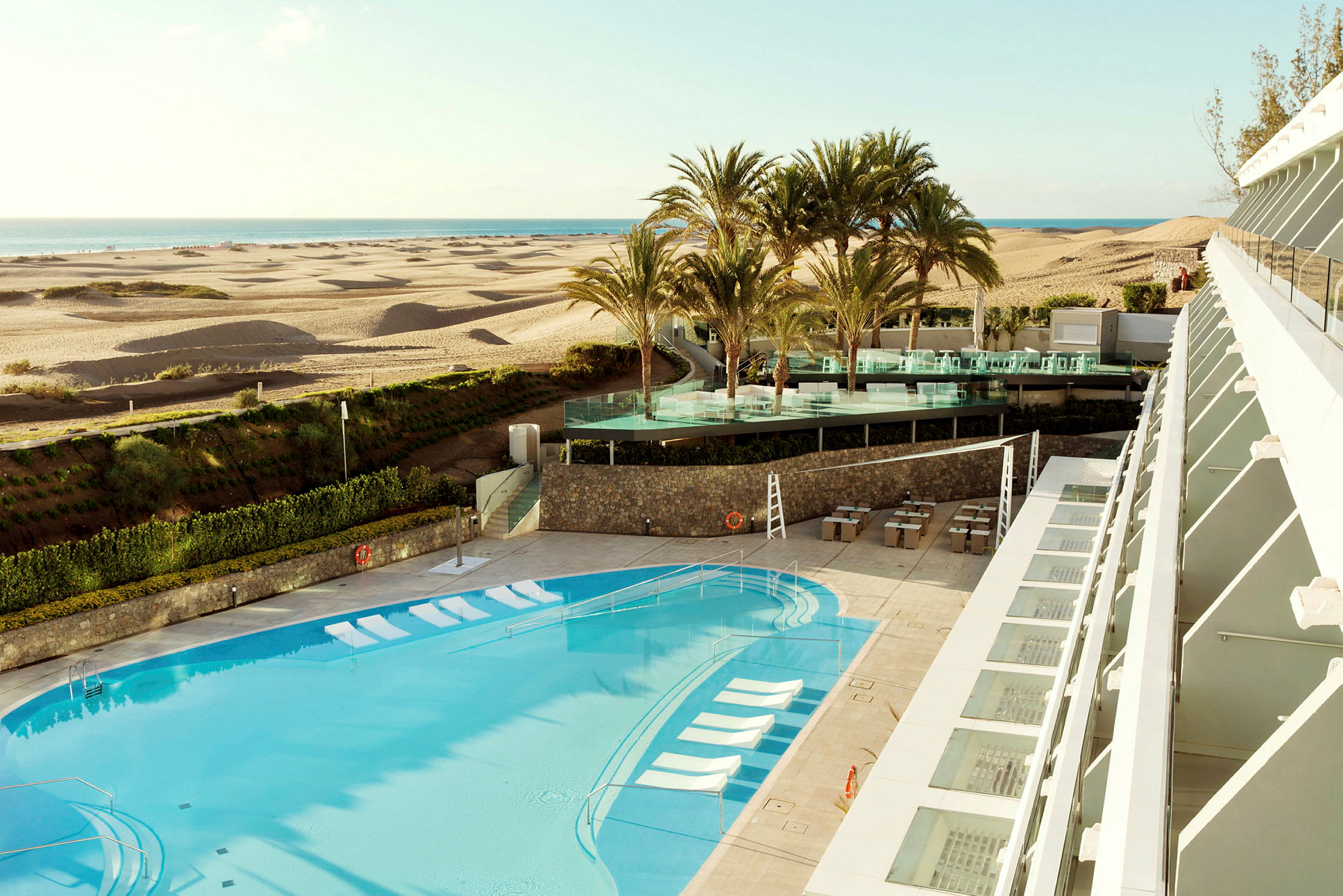 Ett hotell med pool och utsikt mot sanddyner och hav. (AI-genererad text)