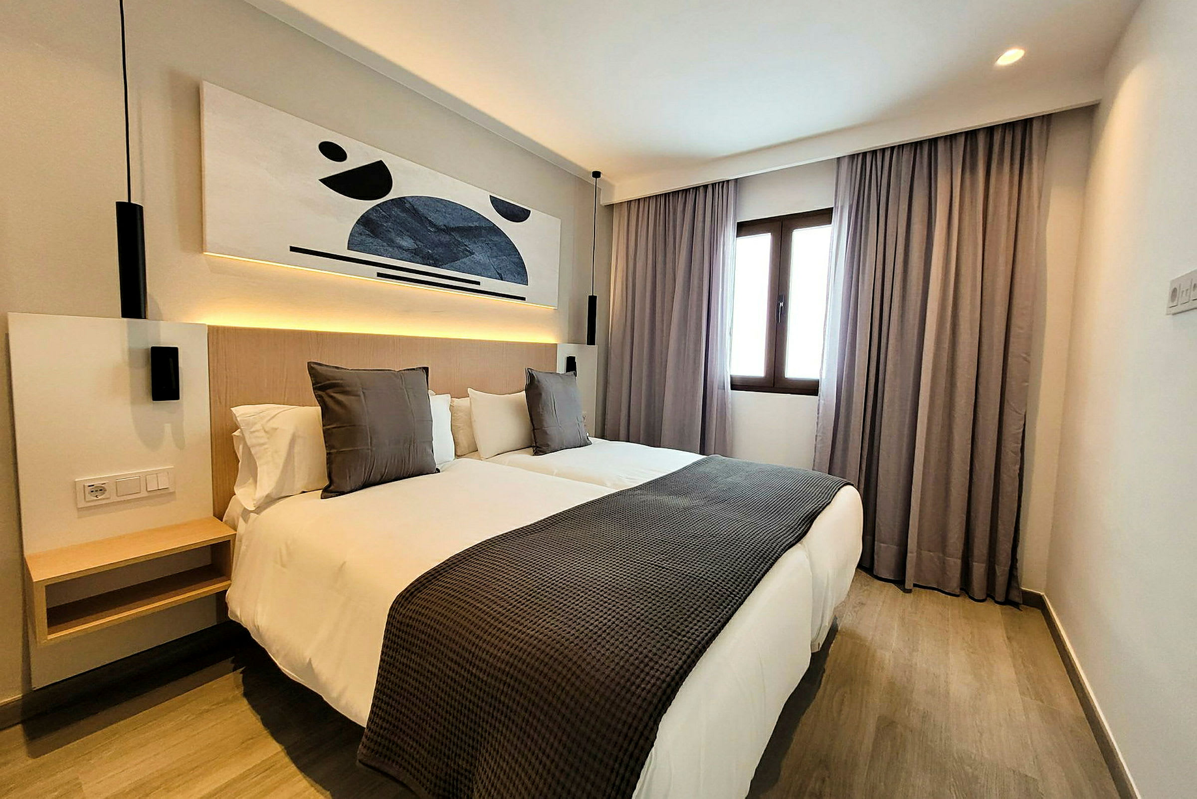 Ett modernt hotellrum med två enkelsängar, konst på väggen och ett fönster med gardiner. (AI-genererad text)