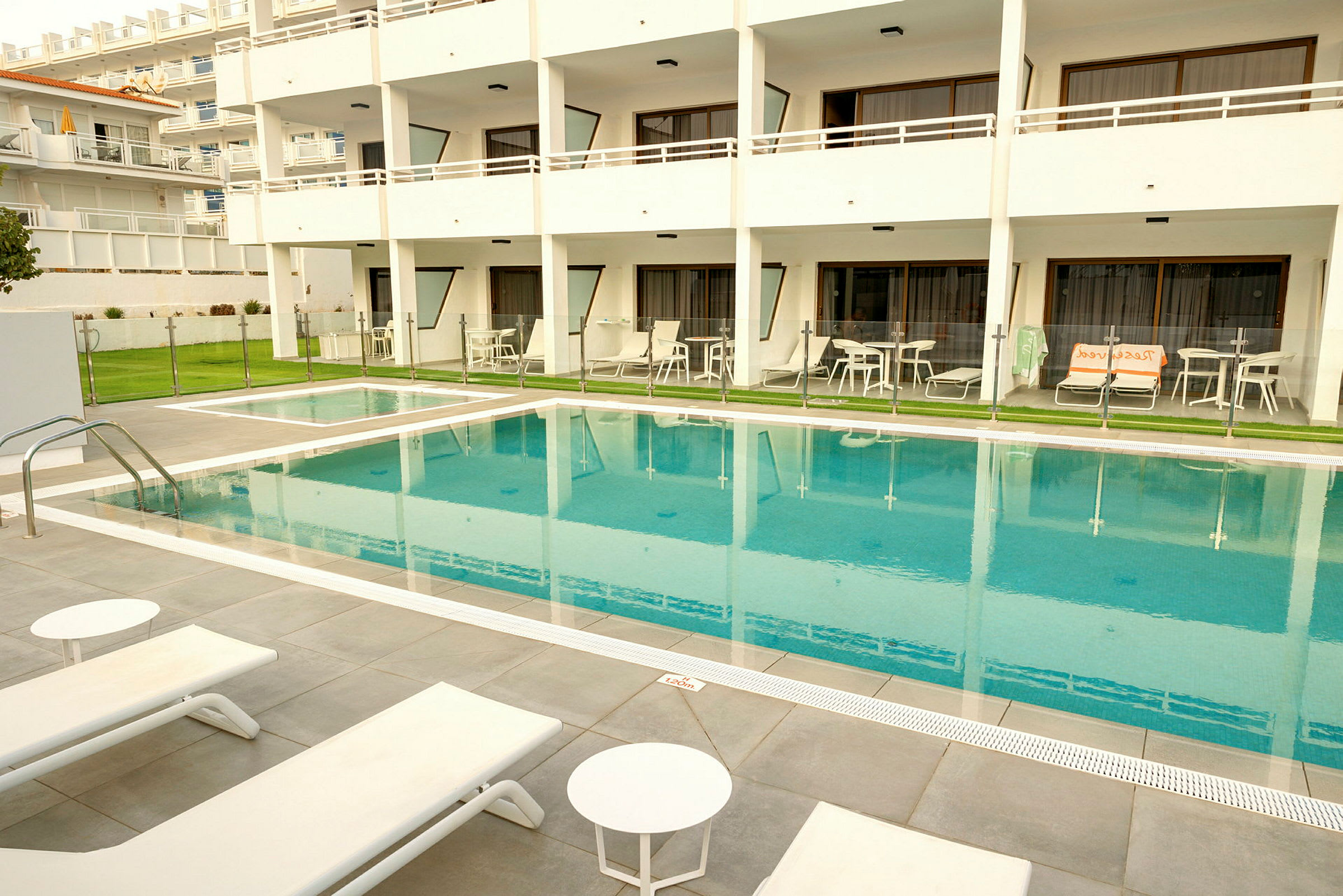 Utomhuspool vid hotell, omgiven av solstolar och bord. (AI-genererad text)