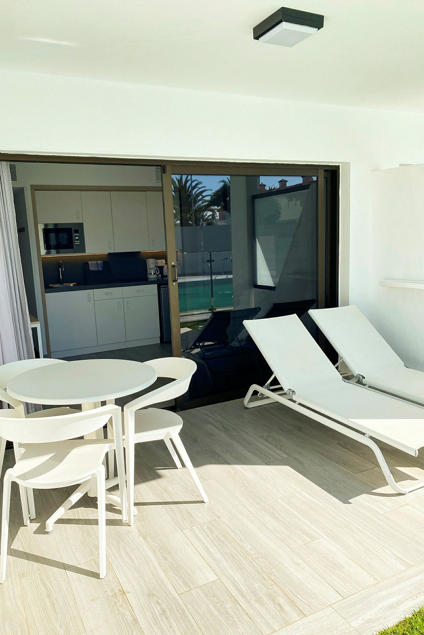 Terrass med bord, stolar, solstolar och utsikt över en köksdel inomhus. (AI-genererad text)