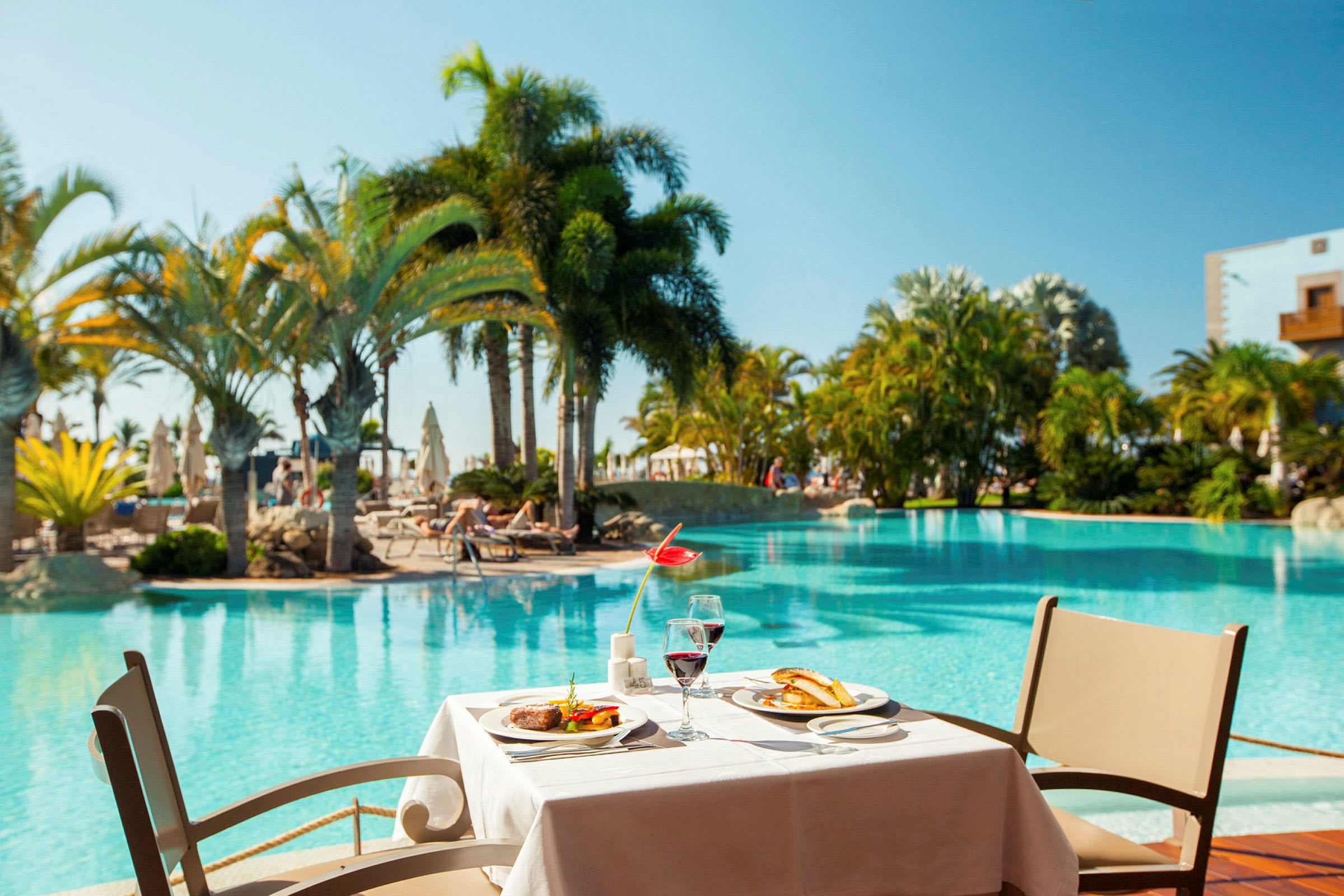En dukad restaurangbordsplats vid en pool med omgivande palmer. (AI-genererad text)