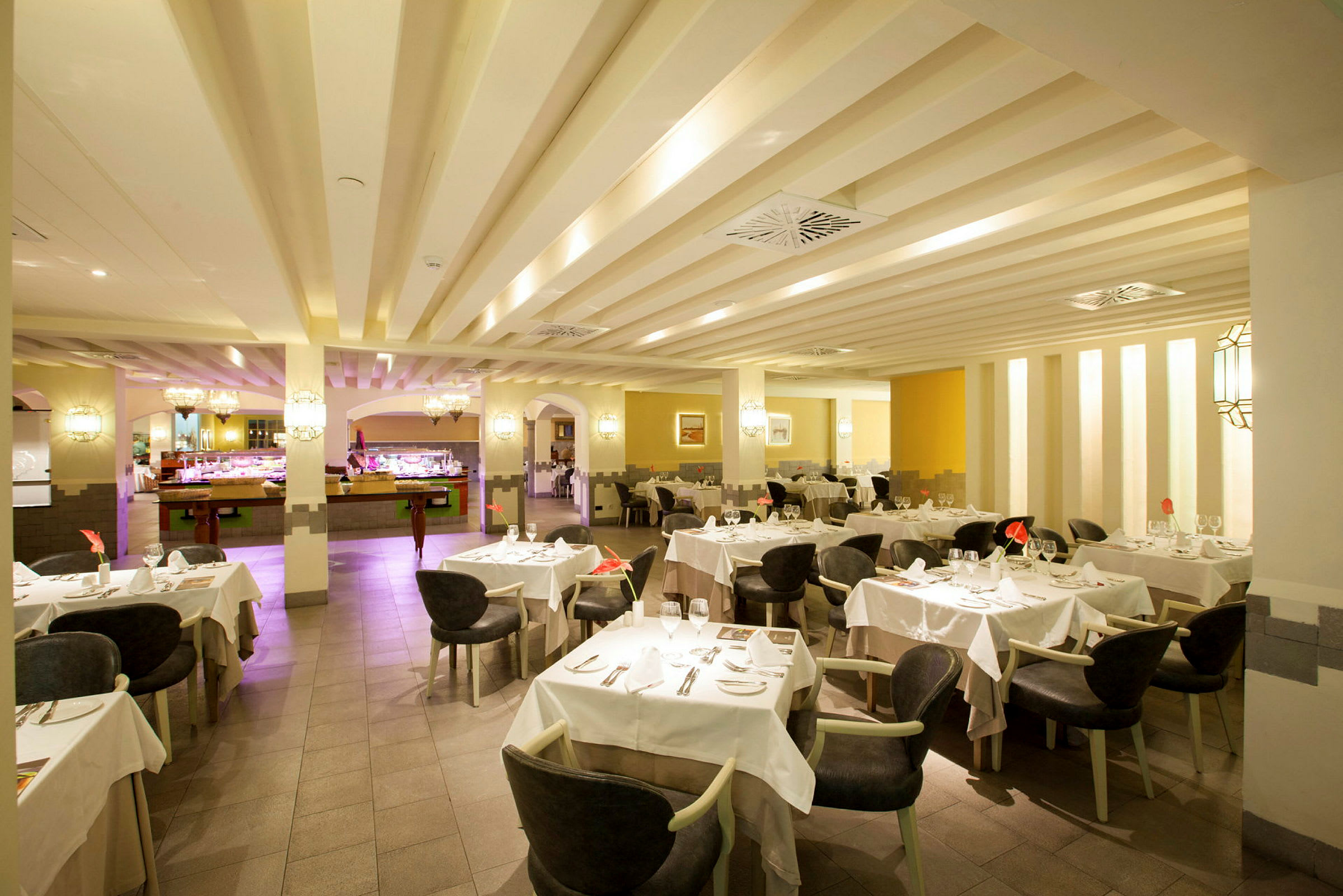En rymlig restaurang med dukade bord och stolar, upplyst interiör med buffédisk i bakgrunden. (AI-genererad text)